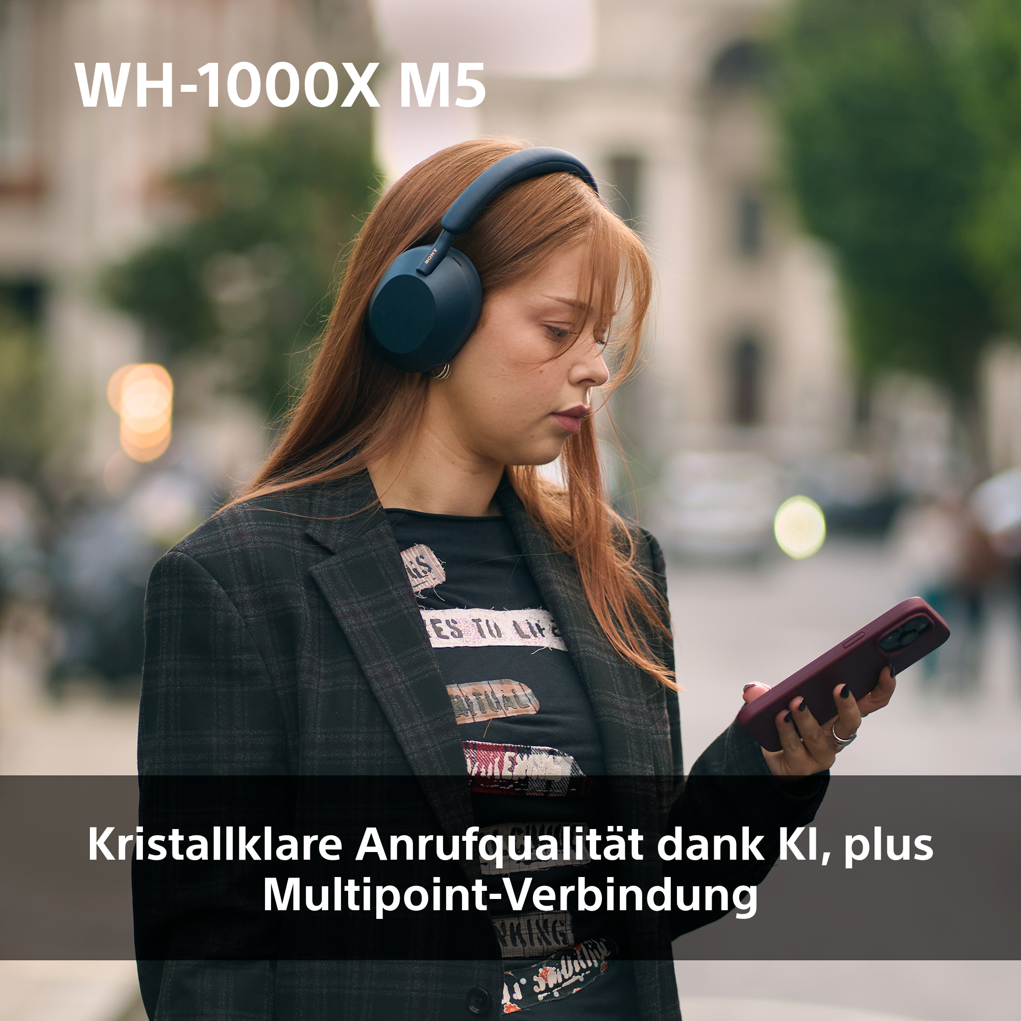 Eine junge Frau mit Kopfhörern betrachtet ihr Handy. Sie trägt eine Jacke, im Hintergrund Bäume und Gebäude verschwommen.