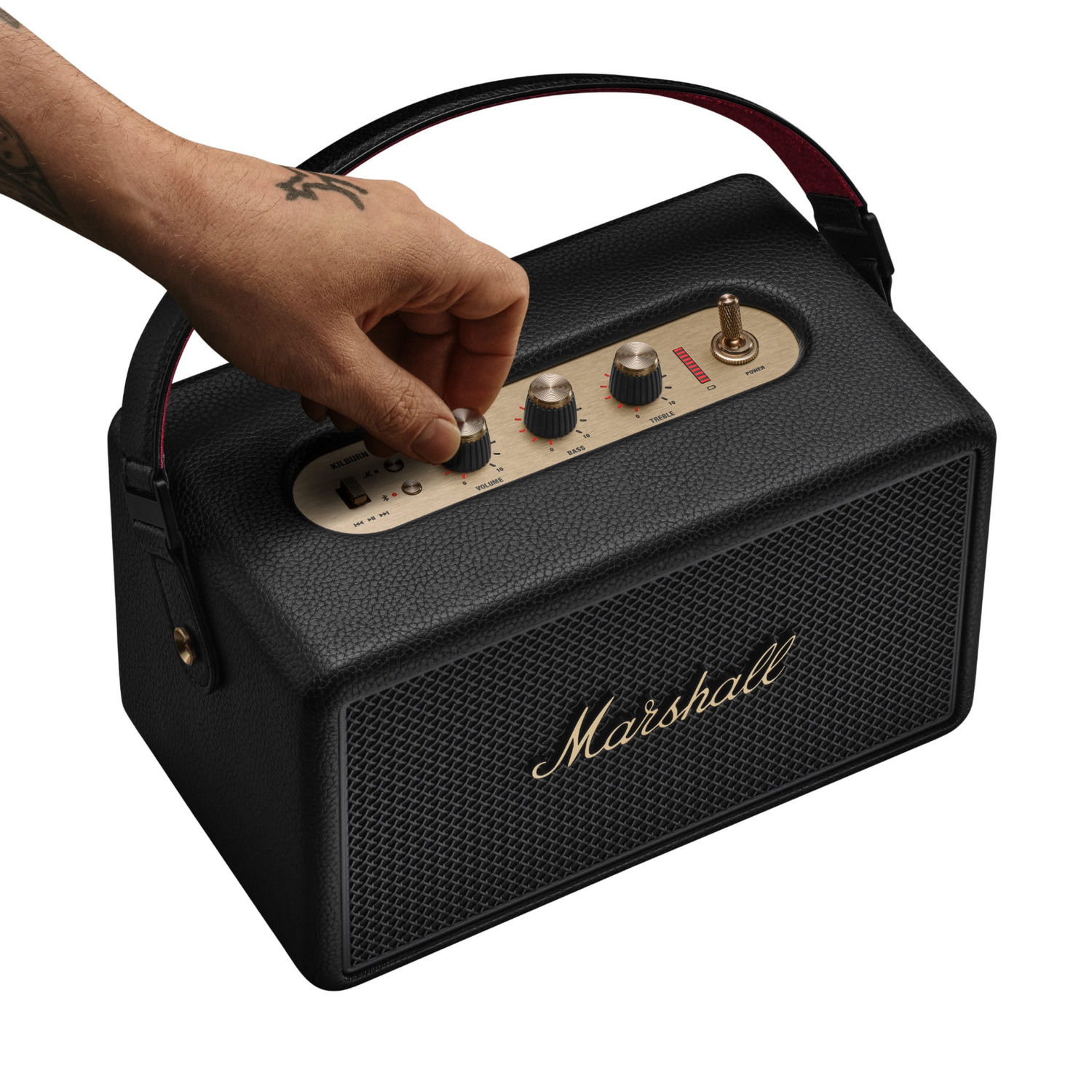 Una mano ajusta la perilla de volumen en un altavoz Marshall negro. El altavoz tiene detalles dorados y un asa forrada en rojo.