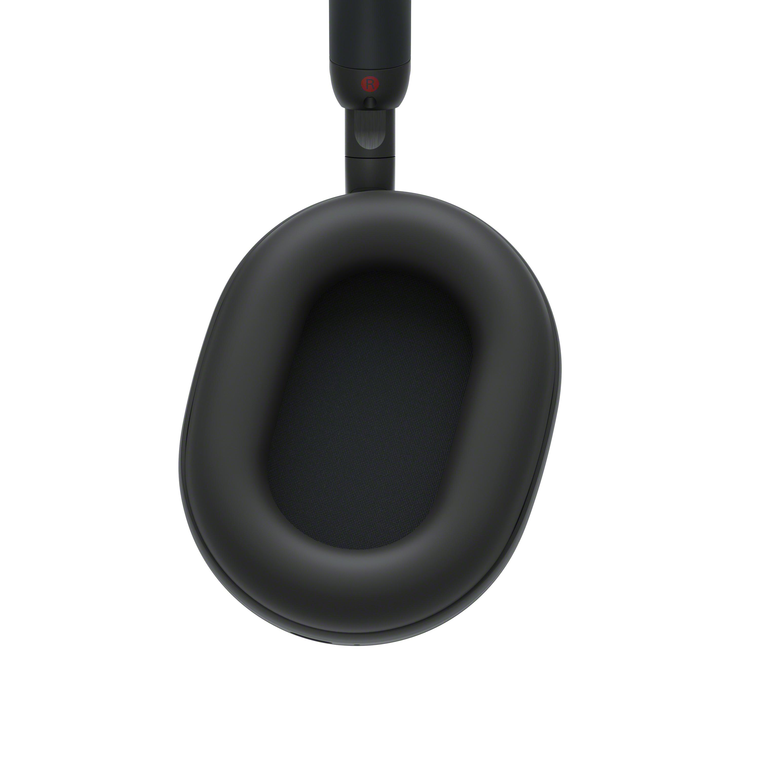 Nahaufnahme eines schwarzen Kopfhörers. Die Ohrmuschel ist oval mit einem Netzeinsatz. Der Kopfbügel ist dunkel und hat ein rotes 'R'-Logo.