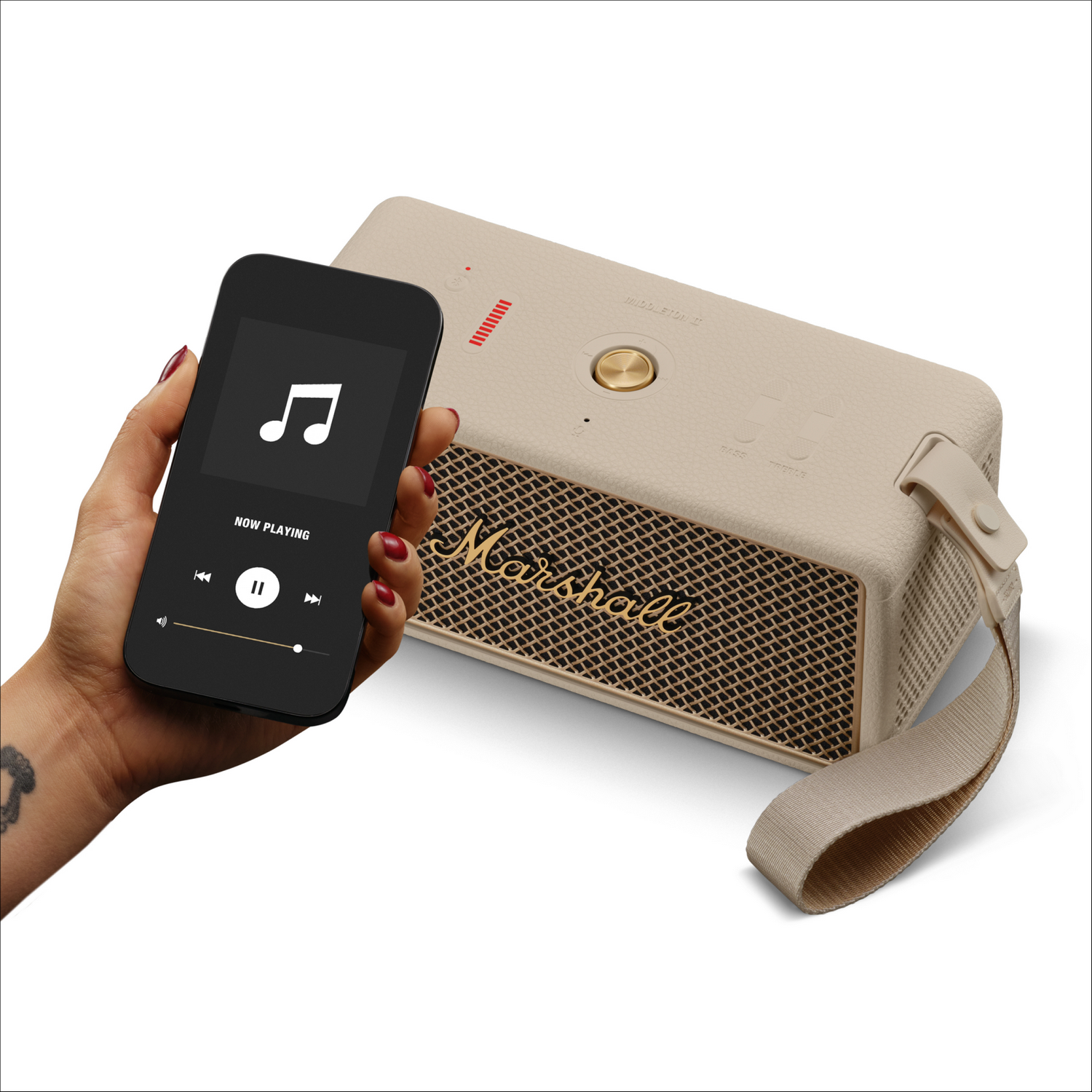 Una mujer sostiene un teléfono que muestra una aplicación de música junto a un altavoz Marshall. El altavoz es beige con rejilla y correa doradas.