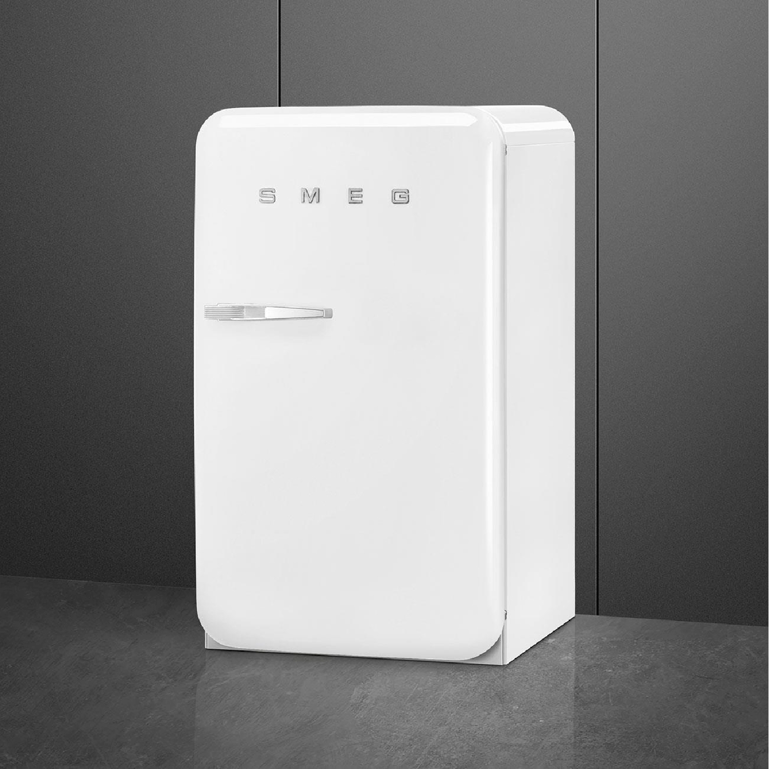 Un frigorifero SMEG bianco. Ha una maniglia cromata e il logo SMEG sulla porta. È contro un muro grigio scuro.