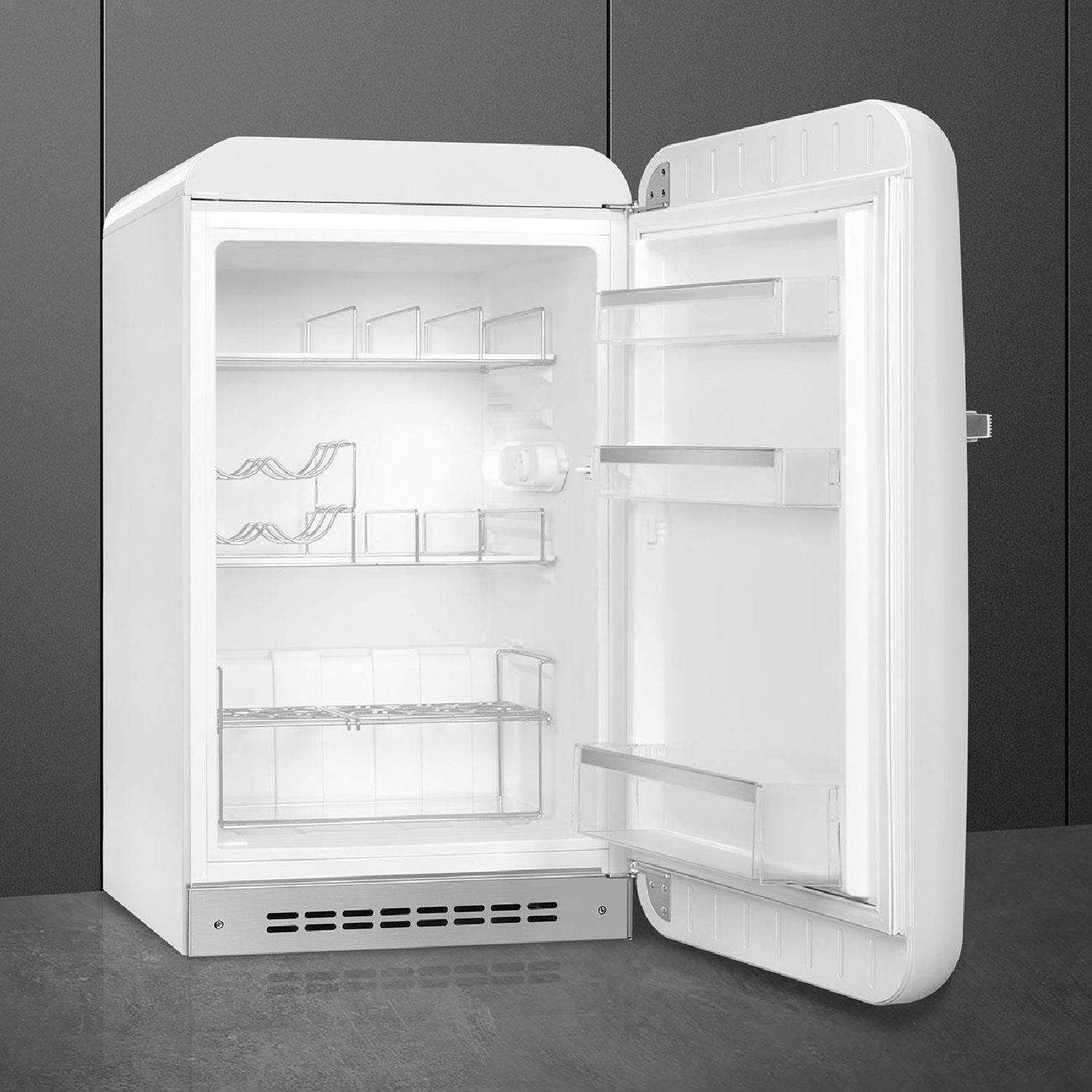 Un frigorifero bianco con la porta aperta. Sono visibili ripiani e rastrelliere interne. Pavimento grigio e parete nera sullo sfondo.