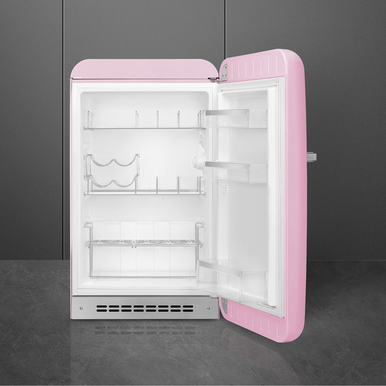 Un frigorifero retrò rosa con la porta aperta. L'interno è bianco, con ripiani e un portabottiglie. Sfondo grigio.