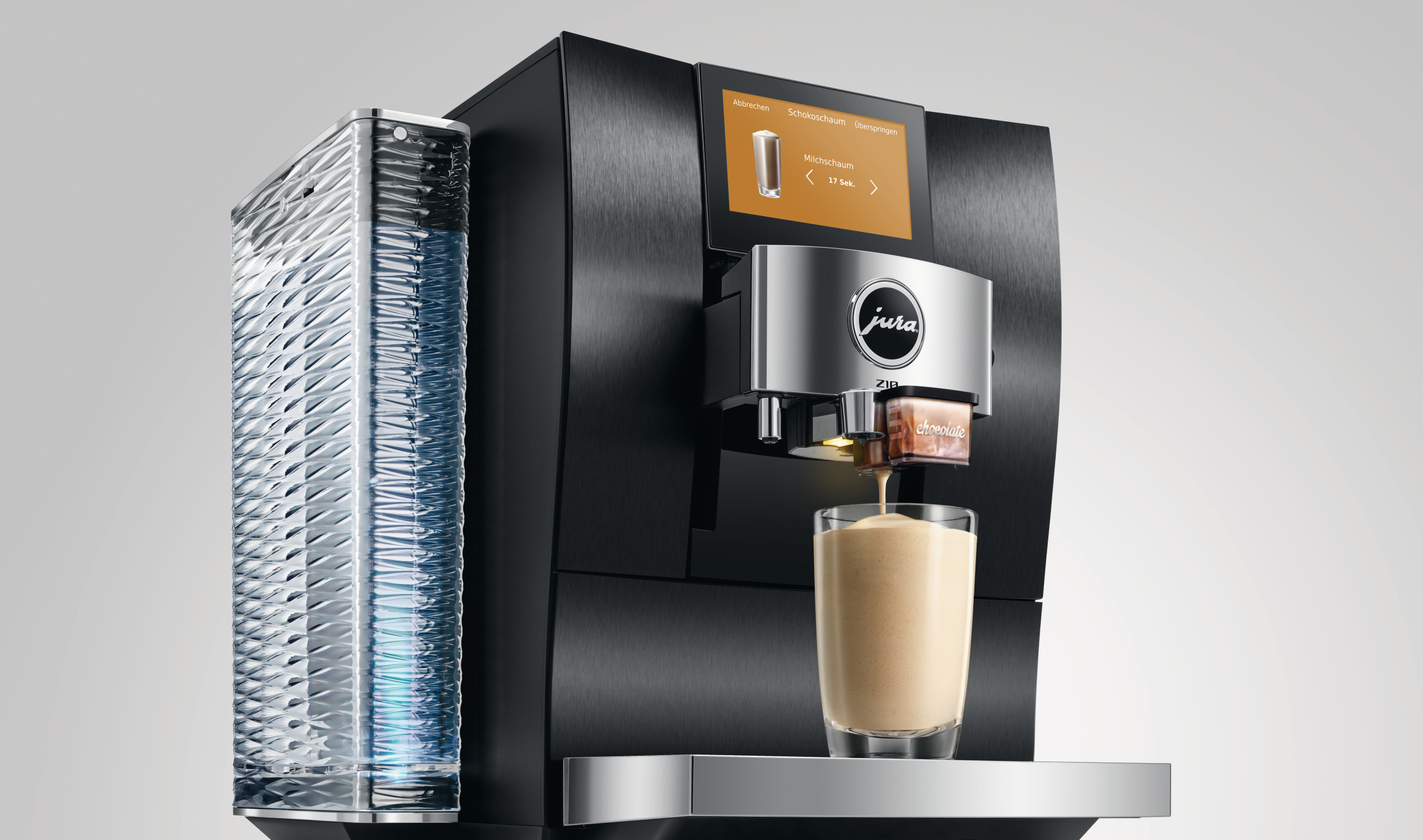 Eine schwarze Kaffeemaschine mit einem Glas Kaffee, das eingegossen wird. Links befindet sich ein Milchbehälter. Die Maschine hat einen Bildschirm.