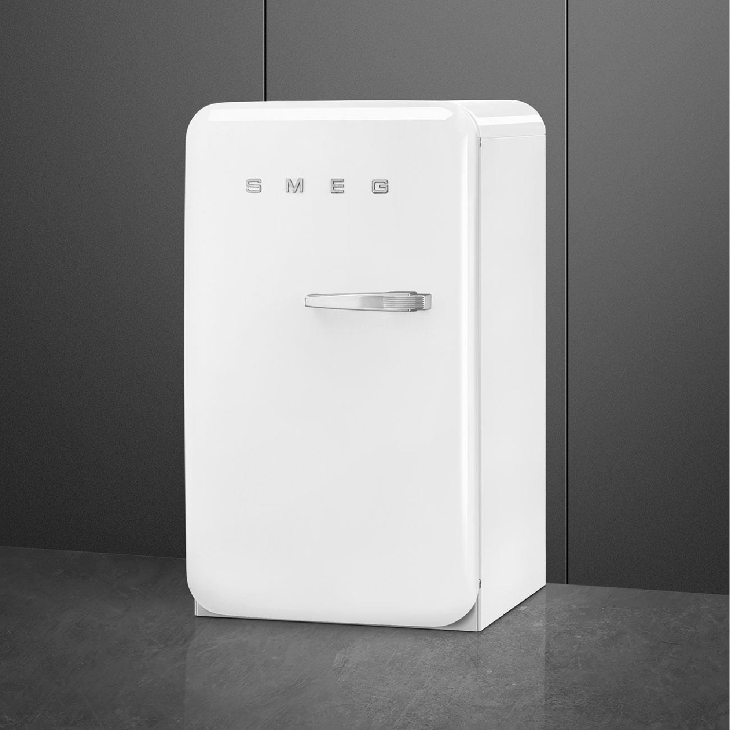 Un frigorifero retrò bianco con la scritta SMEG, maniglia argentata, in piedi davanti a un muro grigio. Pavimento grigio scuro.