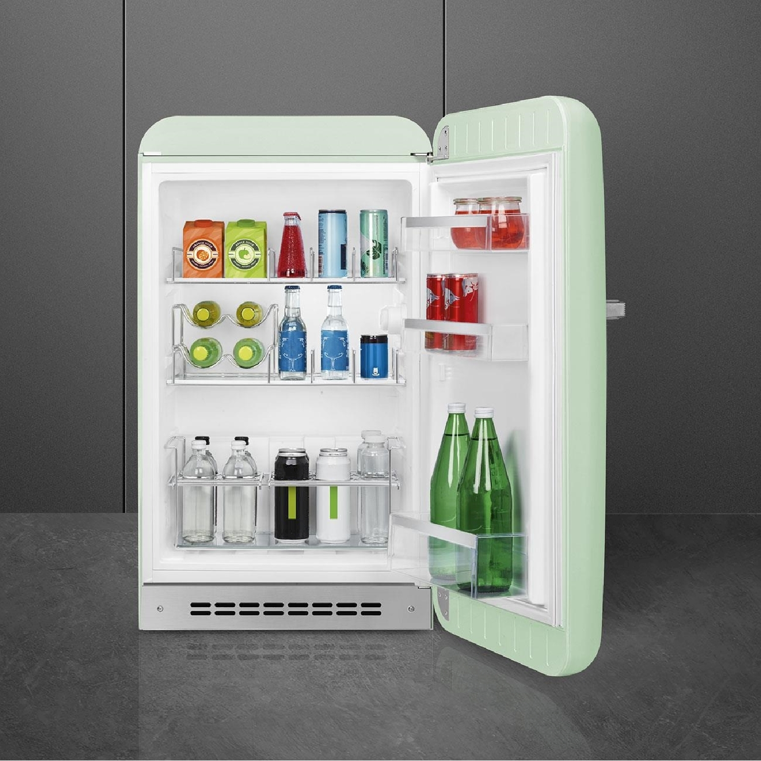Mini-frigorifero verde menta aperto. All'interno ci sono bevande: scatole di succo, bottiglie, lattine e barattoli. Il frigorifero è su un pavimento grigio, contro un muro grigio.