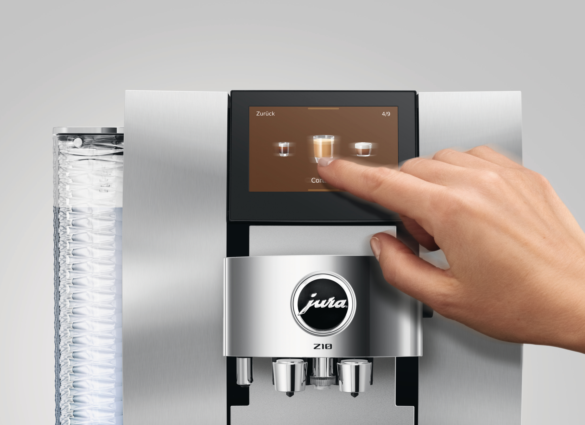 Eine Hand berührt den Bildschirm einer Kaffeemaschine. Der Bildschirm zeigt Kaffeeoptionen. Die Maschine ist silberfarben mit dem Jura-Logo.
