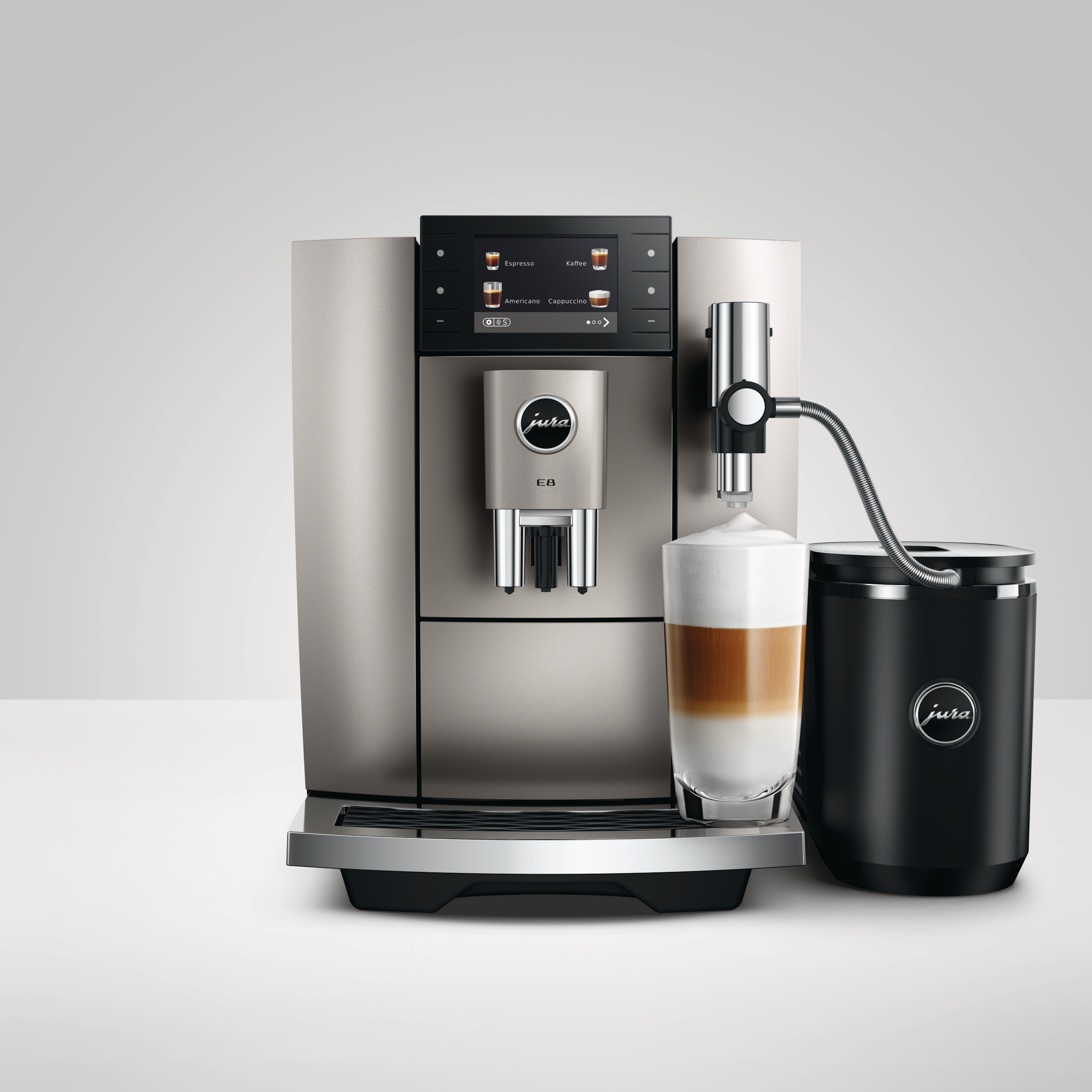 Eine silberne und schwarze Jura E8 Kaffeemaschine mit einem Latte in einem Glas. Rechts ein schwarzer Milchbehälter.
