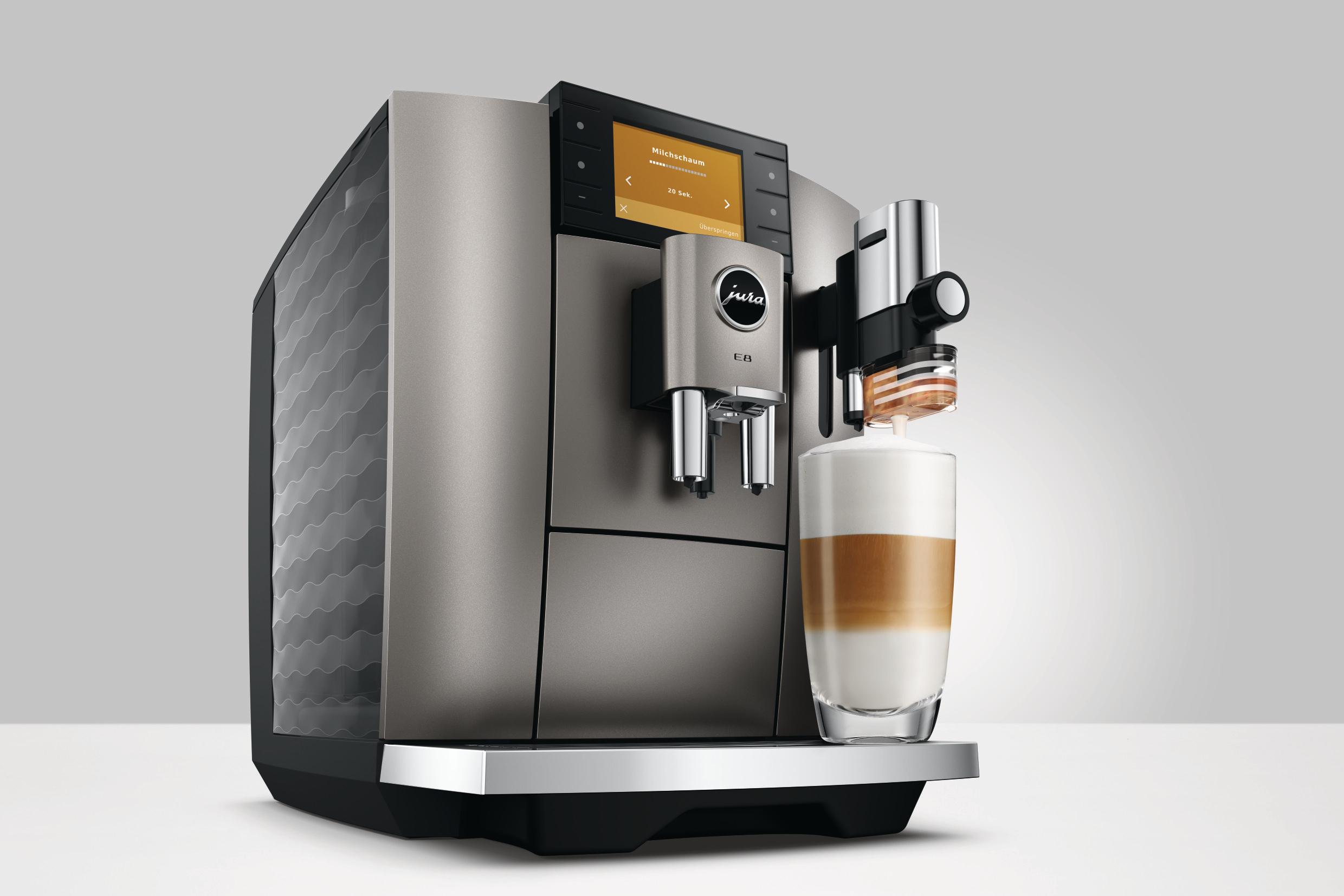 Eine silberne Jura E8 Kaffeemaschine mit Latte Macchiato. Die Maschine hat einen Bildschirm mit Optionen. Ein Kaffeegetränk wird zubereitet.