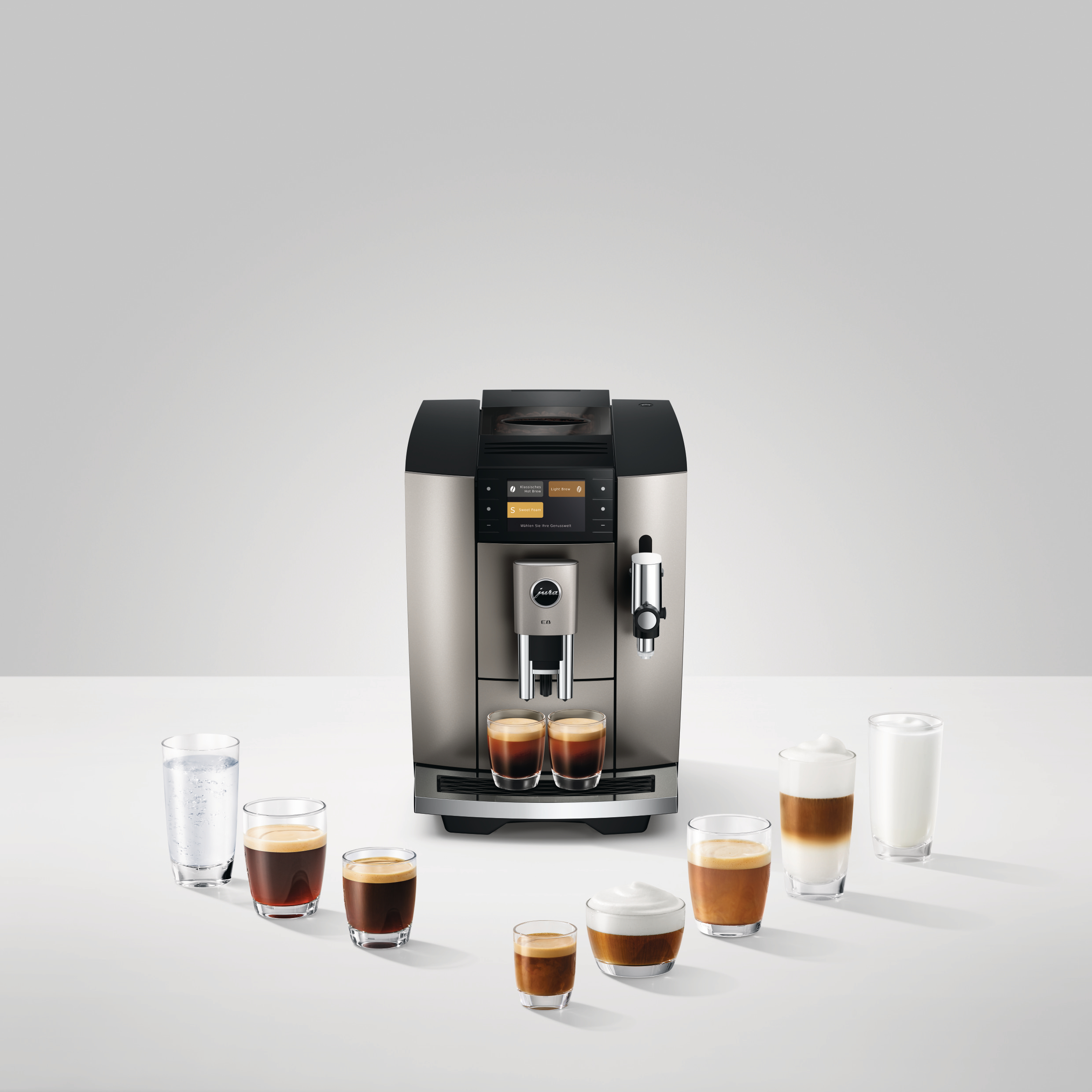 Eine silberne Kaffeemaschine mit Kaffee- und Milchgetränken in Gläsern. Die Maschine steht auf einer weißen Oberfläche, mit weißem Hintergrund.