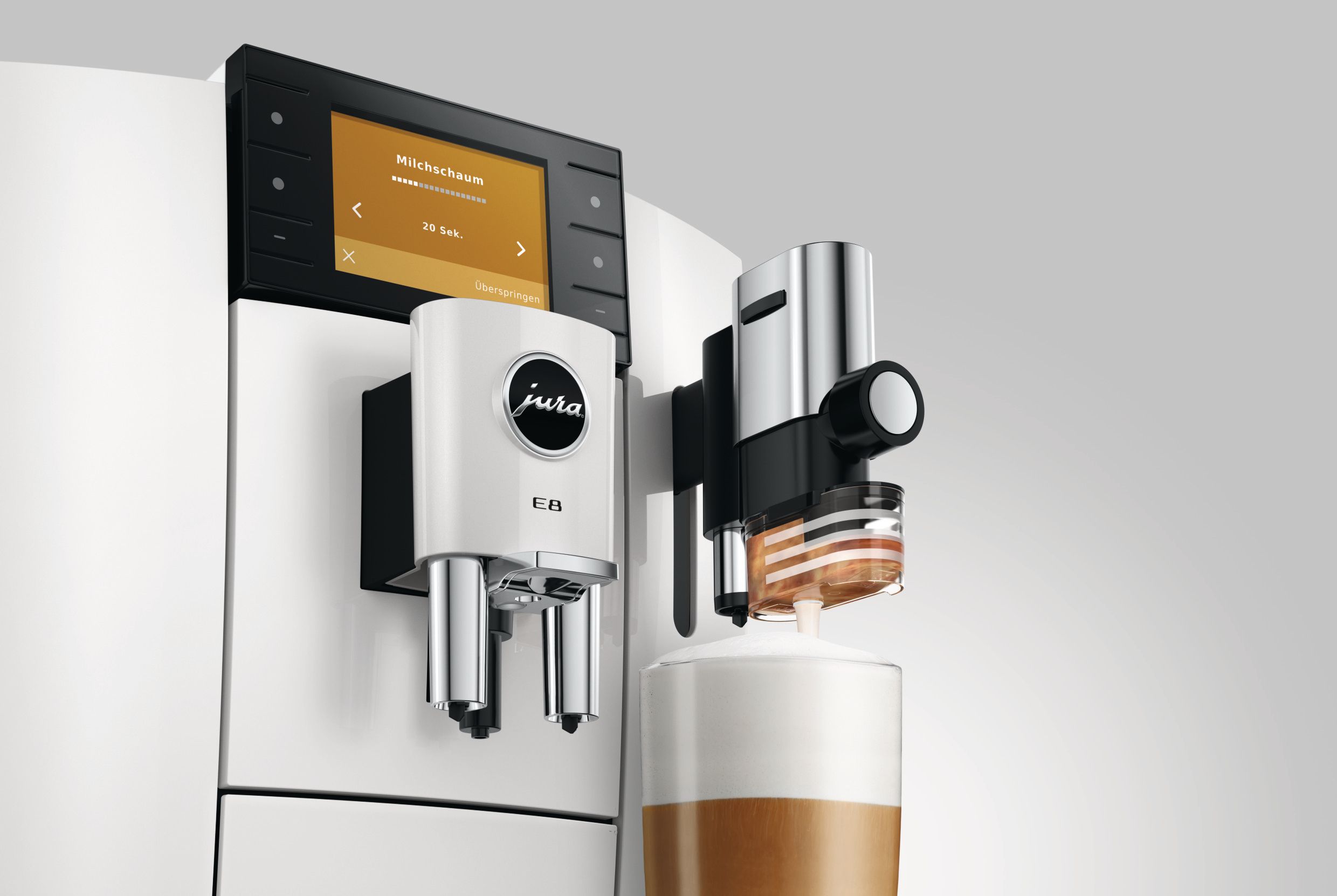 Eine weiße und schwarze Jura E8 Espressomaschine bereitet Milchschaum zu. Ein Glas Kaffee wird gefüllt.