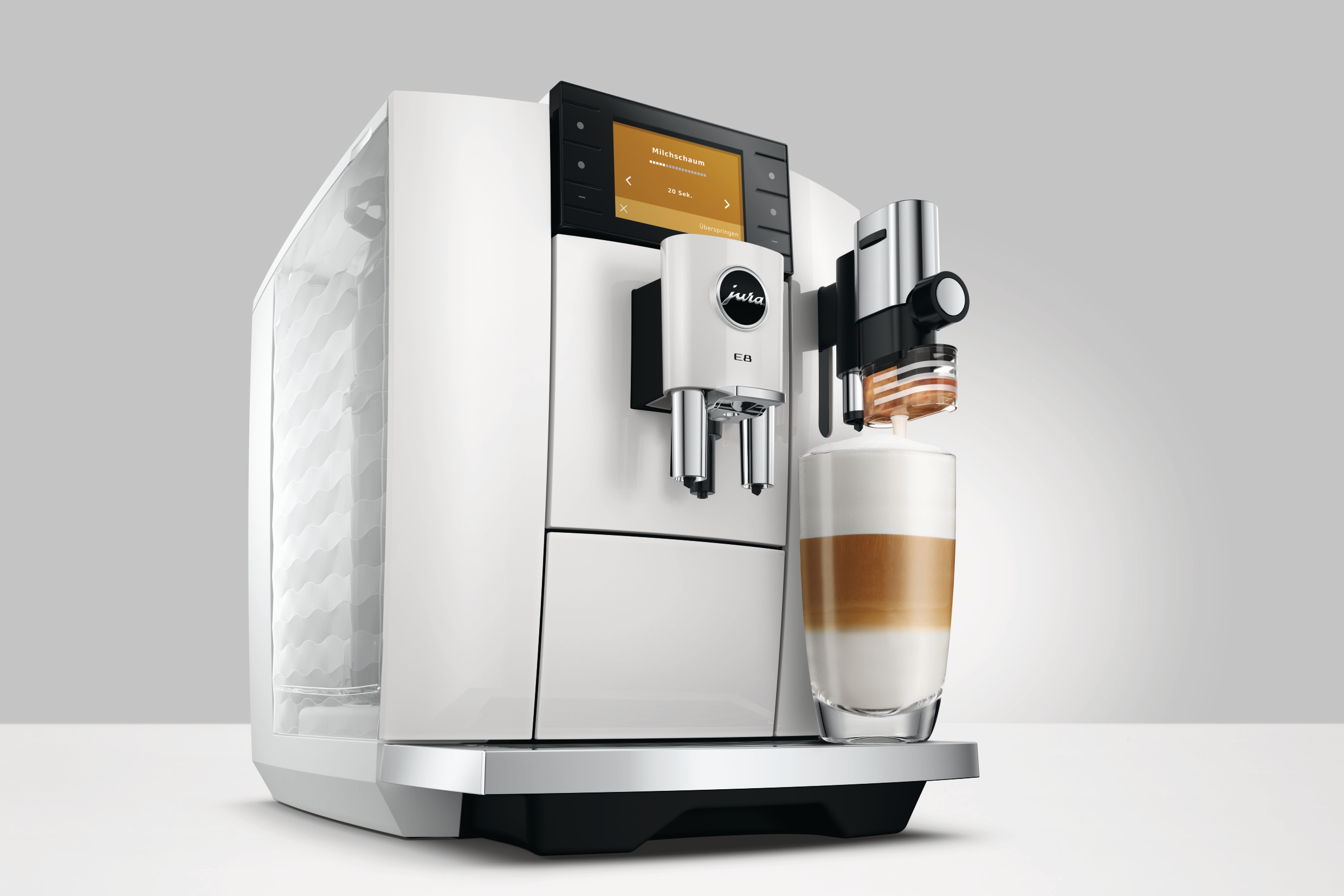 Eine weiße Jura E8 Kaffeemaschine mit einem Glas geschichteten Latte. Die Maschine hat ein Display und Chromakzente.