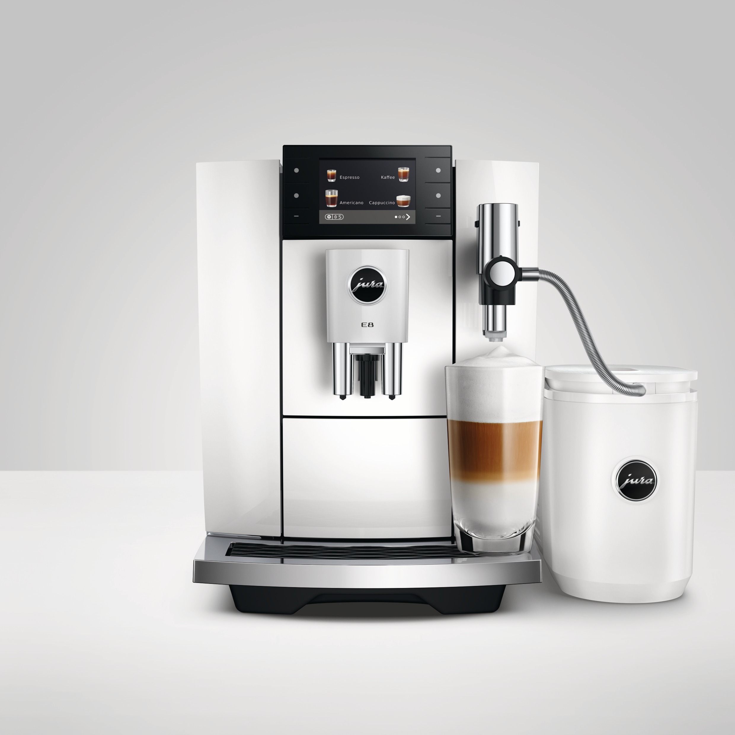 Eine weiße Jura E8 Kaffeemaschine mit einem Glas geschichtetem Latte und einem Milchtank.