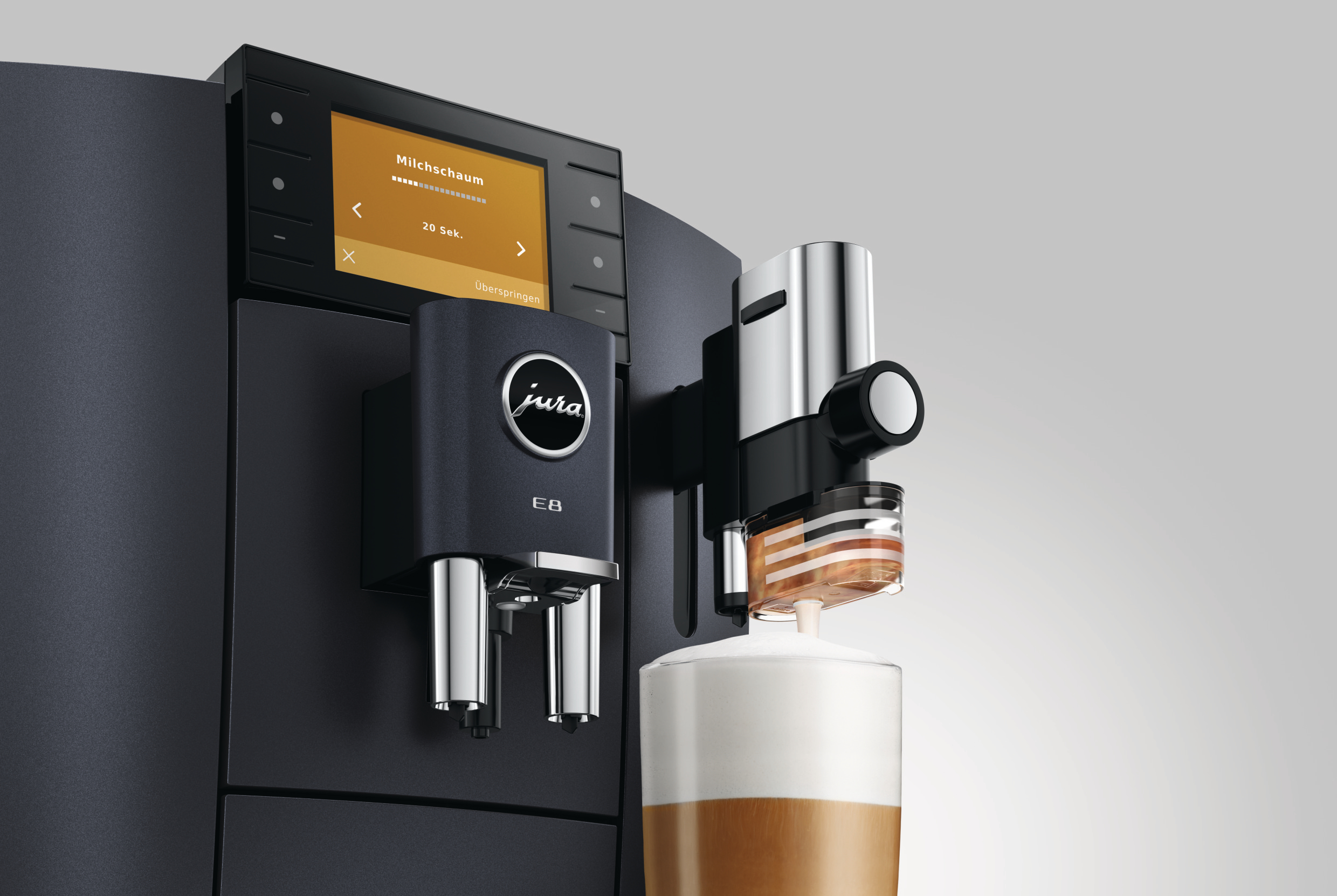 Eine schwarze Jura E8 Espressomaschine mit Milchaufschäumer gibt Kaffee in ein Glas mit Milch- und Kaffeeschichten aus.