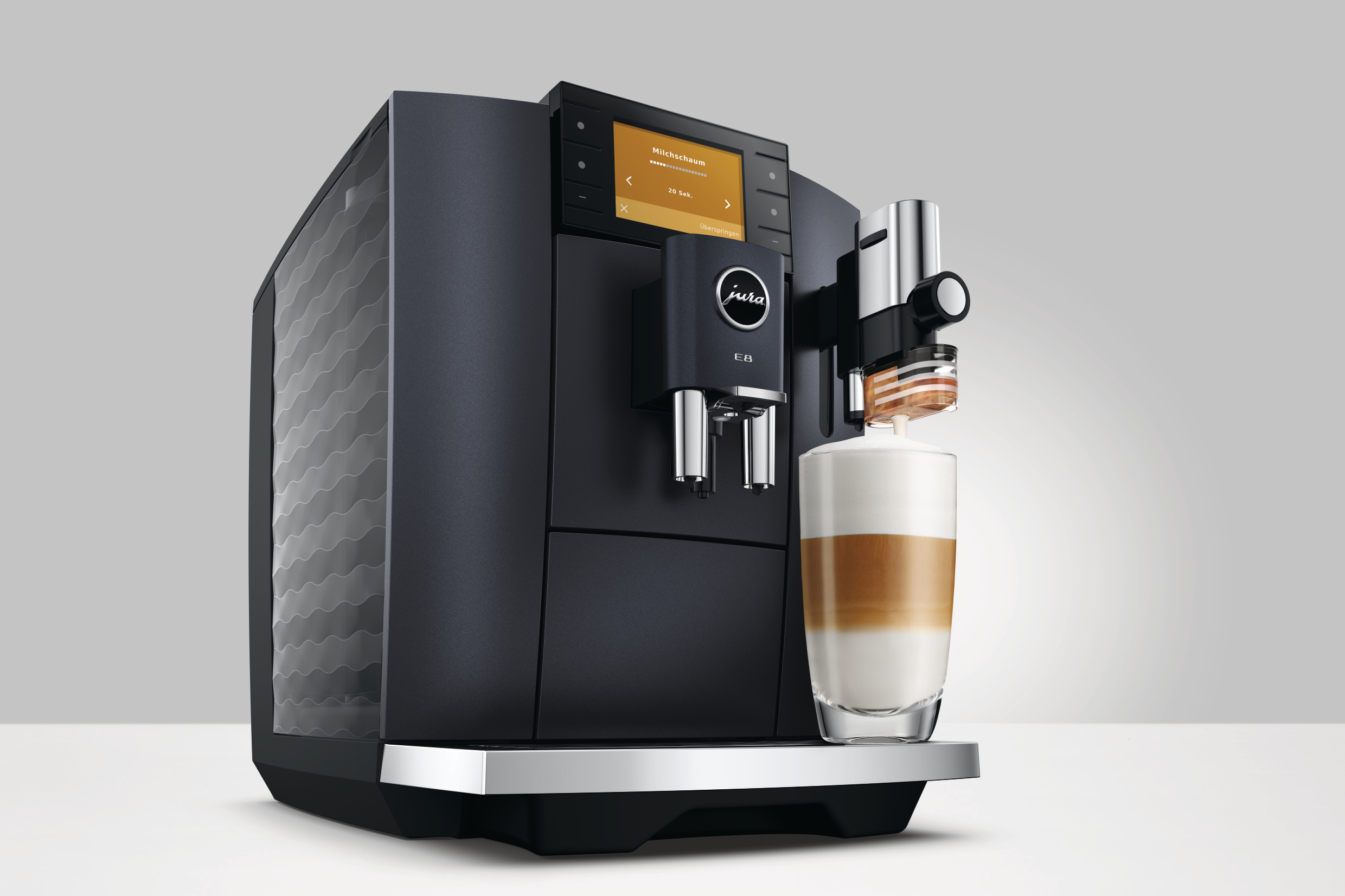 Eine schwarze Kaffeemaschine mit einem Glas geschichteten Latte. Der Bildschirm zeigt Einstellungen. Das Jura-Logo ist sichtbar.