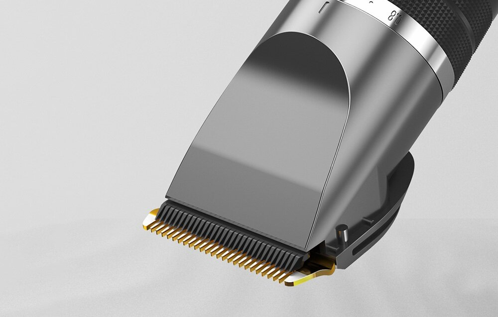 Zbliżenie srebrnej maszynki do włosów. Ostrza są złote. Uchwyt jest czarny i żebrowany. Tło jest jasnoszare.