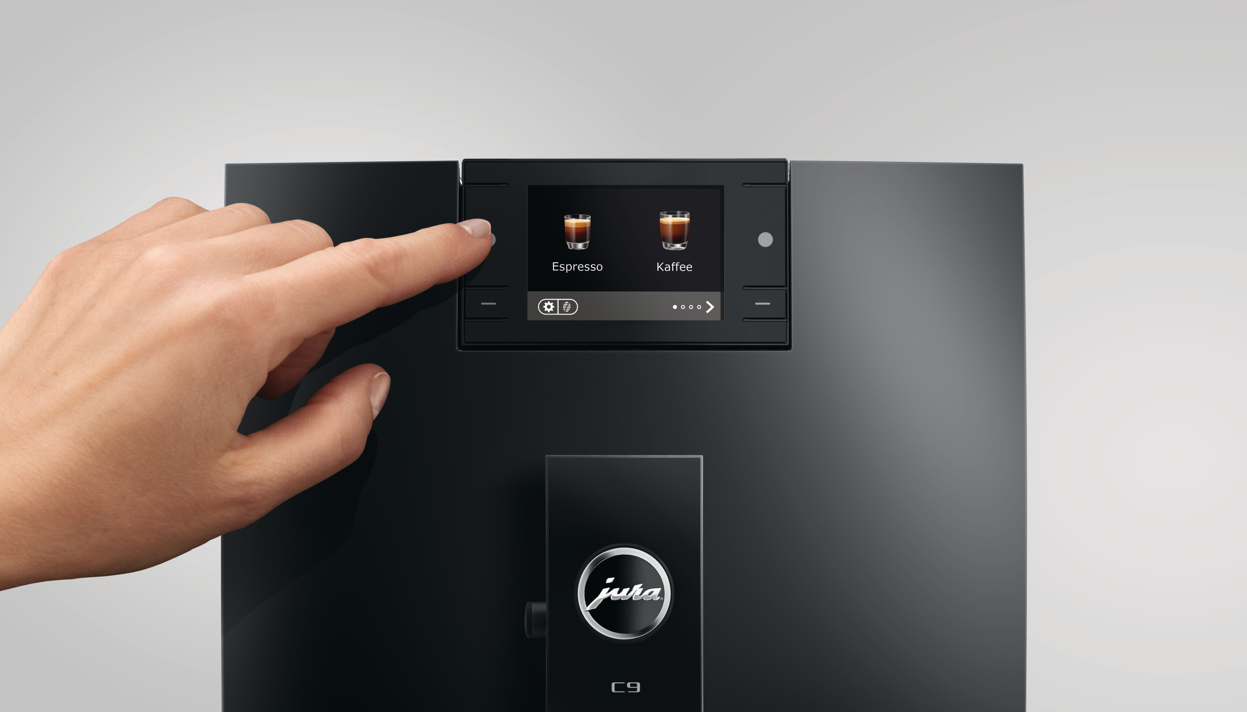 Eine Hand drückt die Espresso-Taste an einer schwarzen Kaffeemaschine. Der Bildschirm zeigt Espresso- und Kaffeeoptionen.