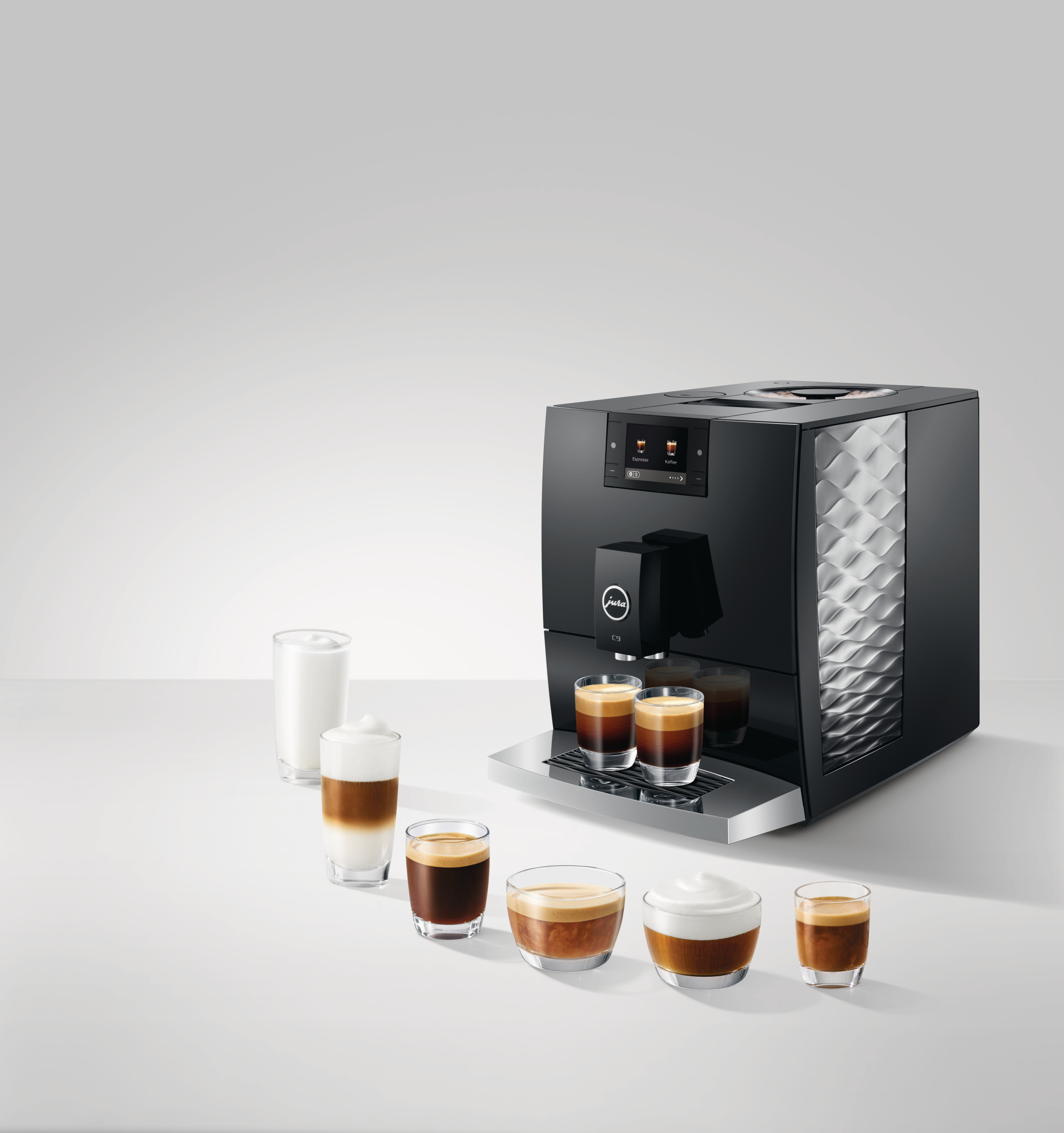 Eine schwarze Kaffeemaschine mit verschiedenen Kaffeegetränken in Gläsern. Die Maschine hat ein silbernes Tablett und ein Display.