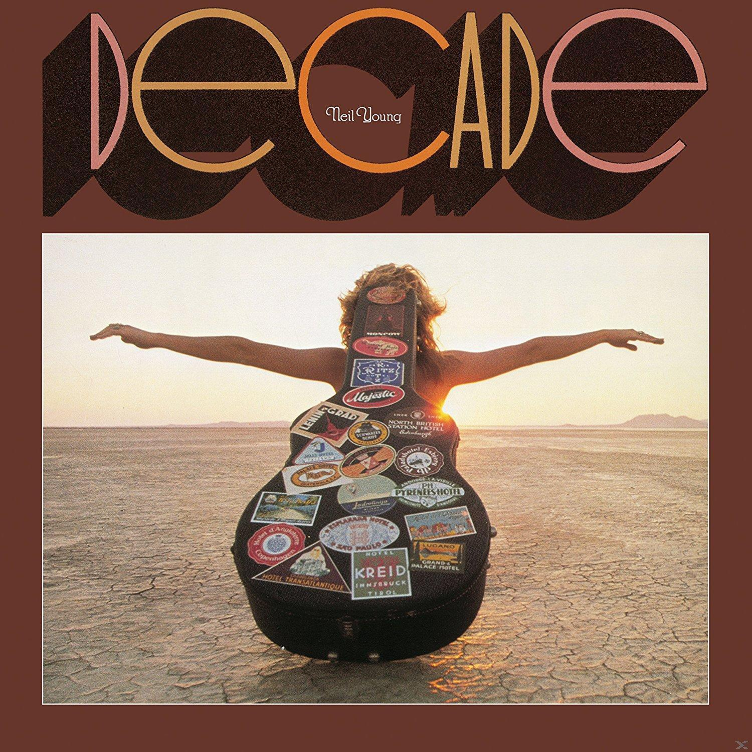 Frau mit ausgestreckten Armen, Gitarrenkoffer auf dem Rücken, steht auf rissiger Erde. Titel 'Decade' oben. Neil Young steht oben.