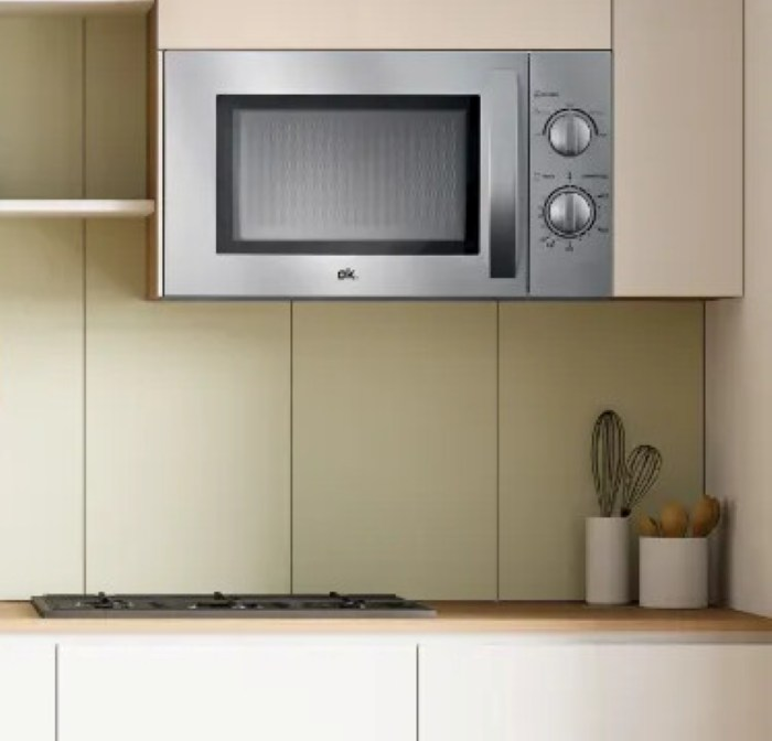 Kuchenka mikrofalowa ze stali nierdzewnej jest wbudowana w szafkę kuchenną. Poniżej znajduje się blat z kuchenką i elementami dekoracyjnymi.