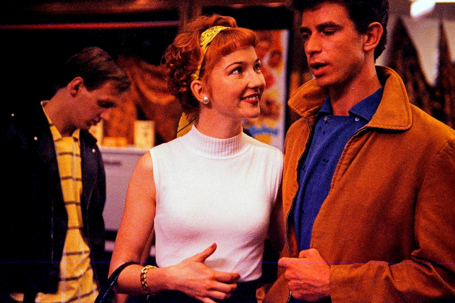 Drei Personen in Retro-Kleidung. Eine Frau in einem weißen Oberteil, ein Mann in einer braunen Jacke und ein anderer Mann in einer schwarzen Jacke, alle lächeln.