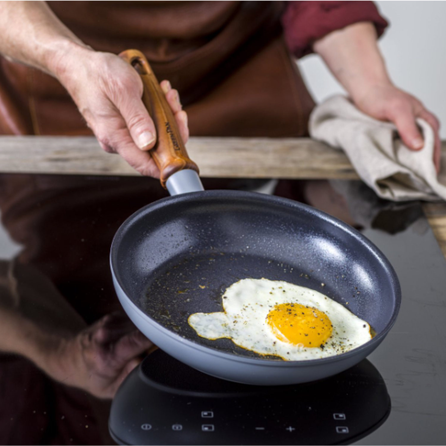 A person cooks a fried egg in a pan. The egg yolk is yellow, and the white is cooked. The pan sits on a black stove.