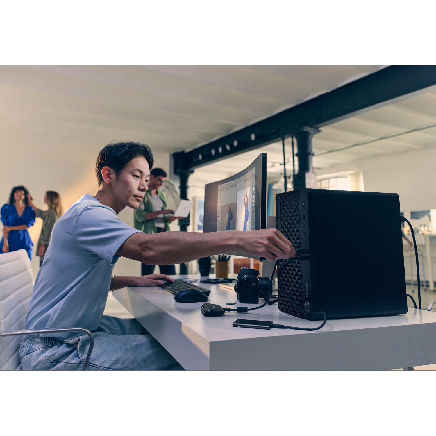 Een man sluit een USB aan op een computer. Hij zit aan een wit bureau met een monitor, toetsenbord en andere apparaten.