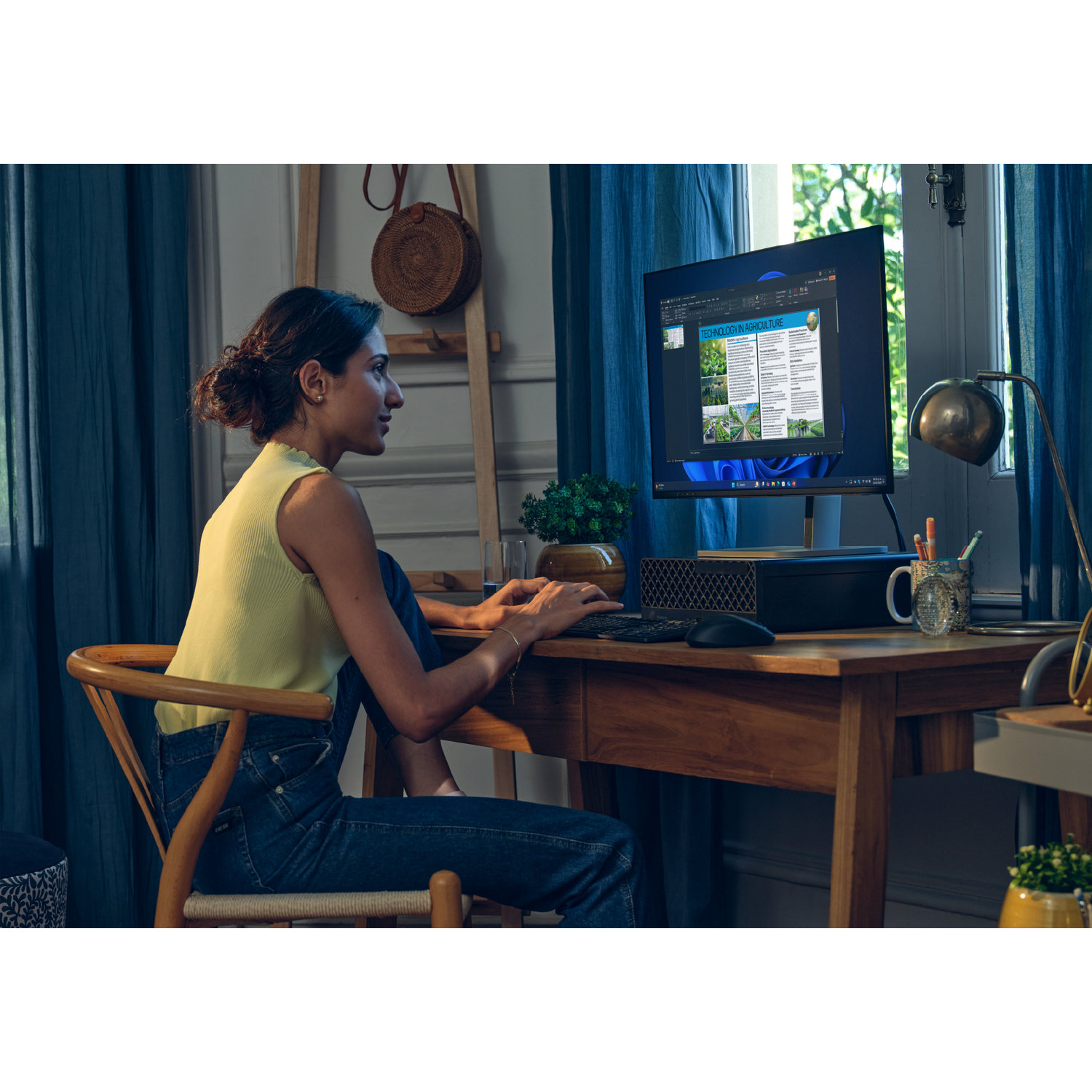 Woman at desk, working on a computer. Monitor displays a document. Desk has a keyboard, mouse, mug, and lamp. Window and curtains.
