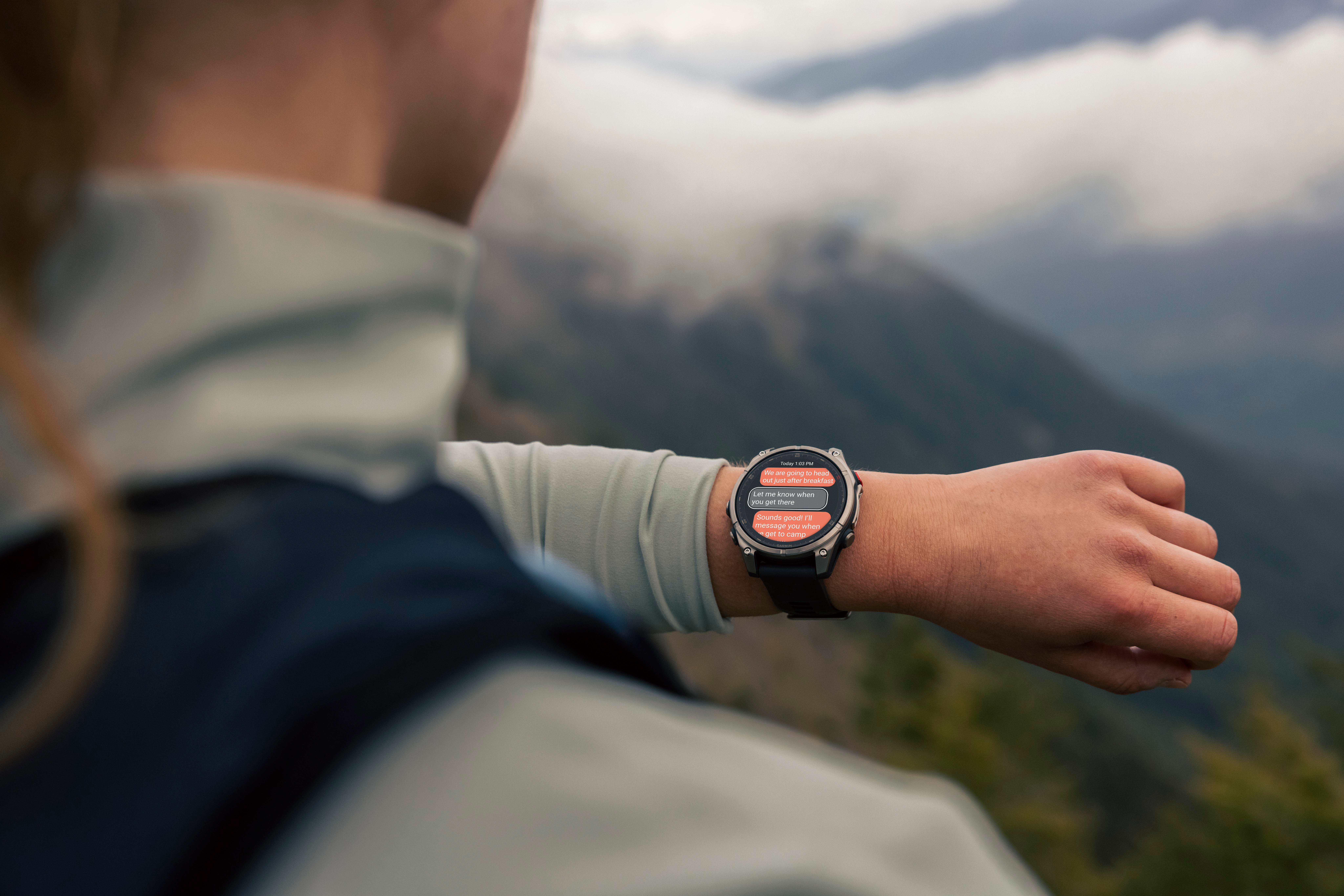 Eine Person trägt eine Smartwatch im Freien. Die Uhr zeigt eine Textnachricht an. Im verschwommenen Hintergrund sind Berge zu sehen.