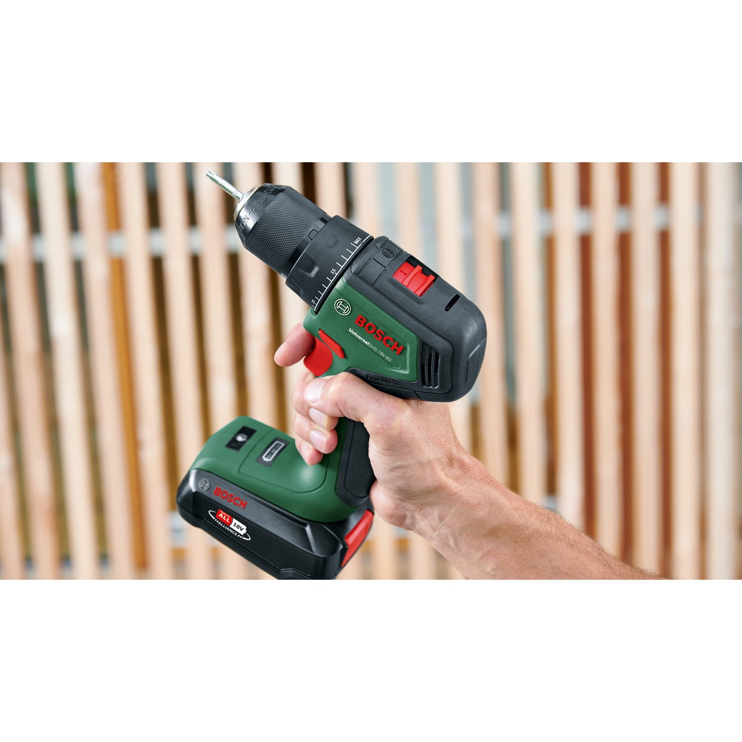 Una mano che tiene un trapano Bosch verde e nero. Lo sfondo presenta pannelli di legno. Il trapano è inclinato verso l'alto a sinistra.