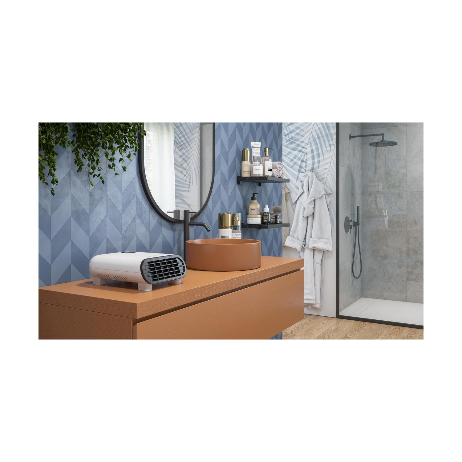 Bagno con mobile marrone, lavabo e specchio. Un termoventilatore bianco sul mobile. Doccia e mensole con prodotti visibili.