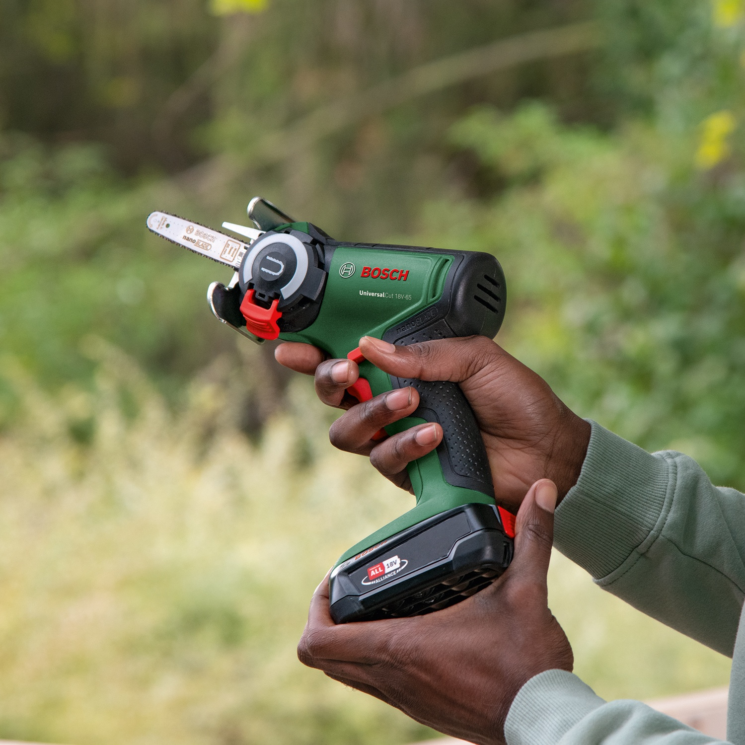 Una persona tiene in mano un Bosch UniversalCut 18V-65 verde e nero. L'utensile ha un pulsante rosso e una piccola lama per sega.