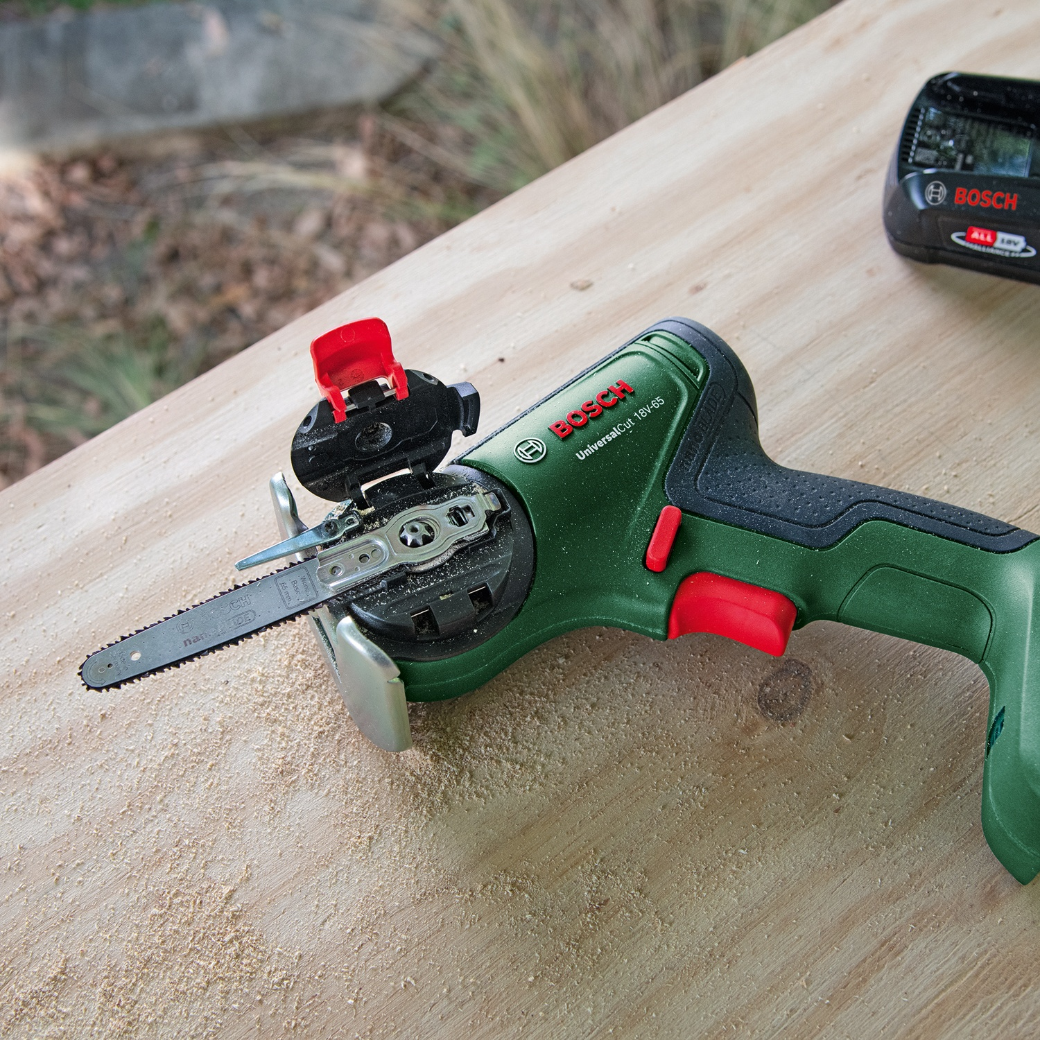 Una sega Bosch UniversalCut 18V-65 verde e nera su legno. Una batteria è dietro. Segatura sul legno.