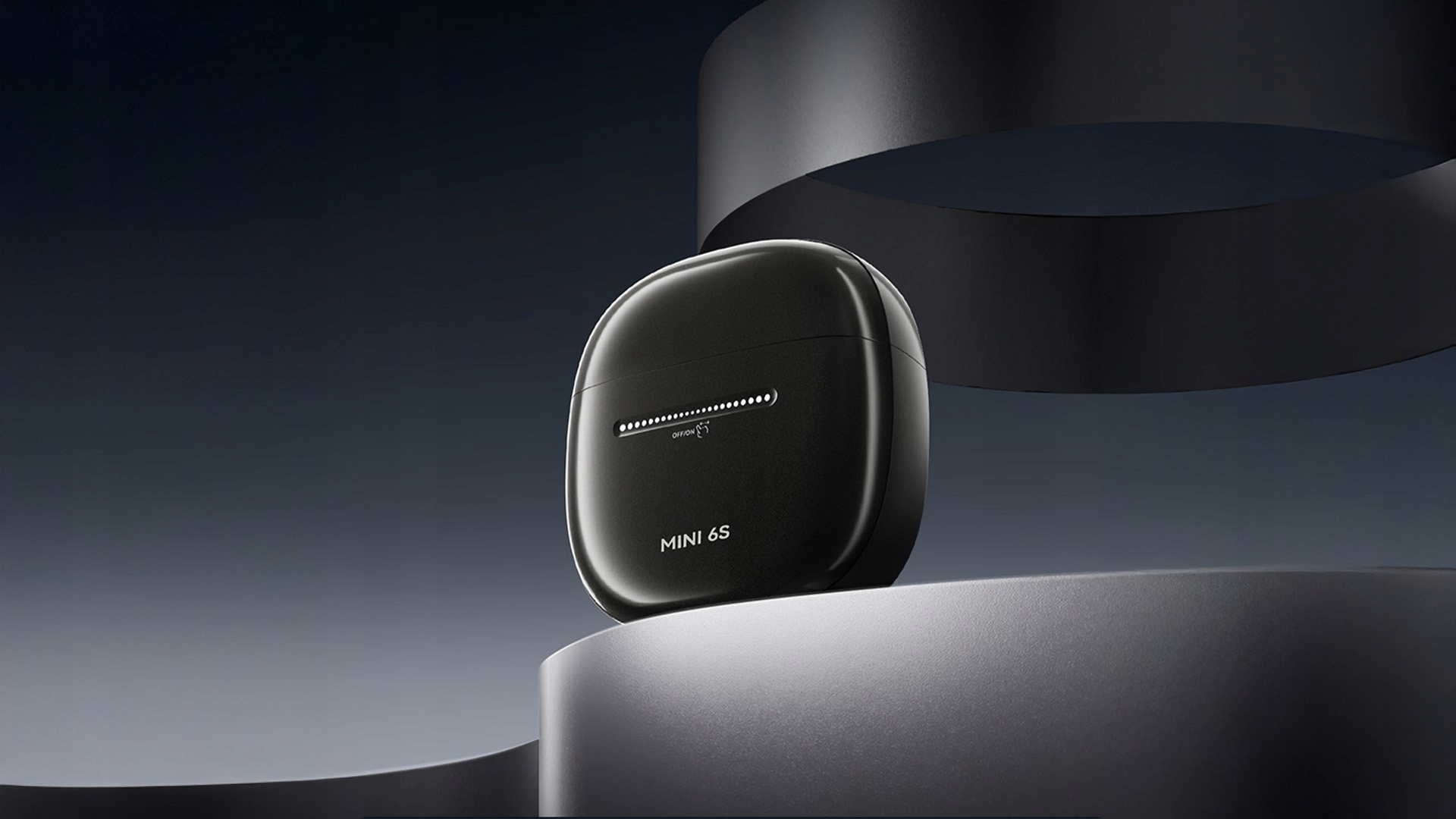 Czarne, zaokrąglone etui na słuchawki z napisem 'MINI 6S' na cokole. Ciemne tło z zakrzywionym czarnym kształtem.