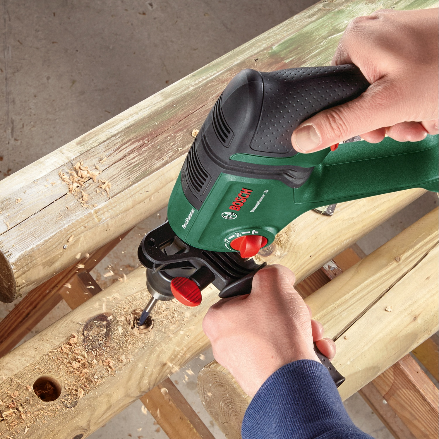 Una persona fora un buco nel legno con un trapano Bosch verde e nero. Segatura visibile. Mani che impugnano il trapano.