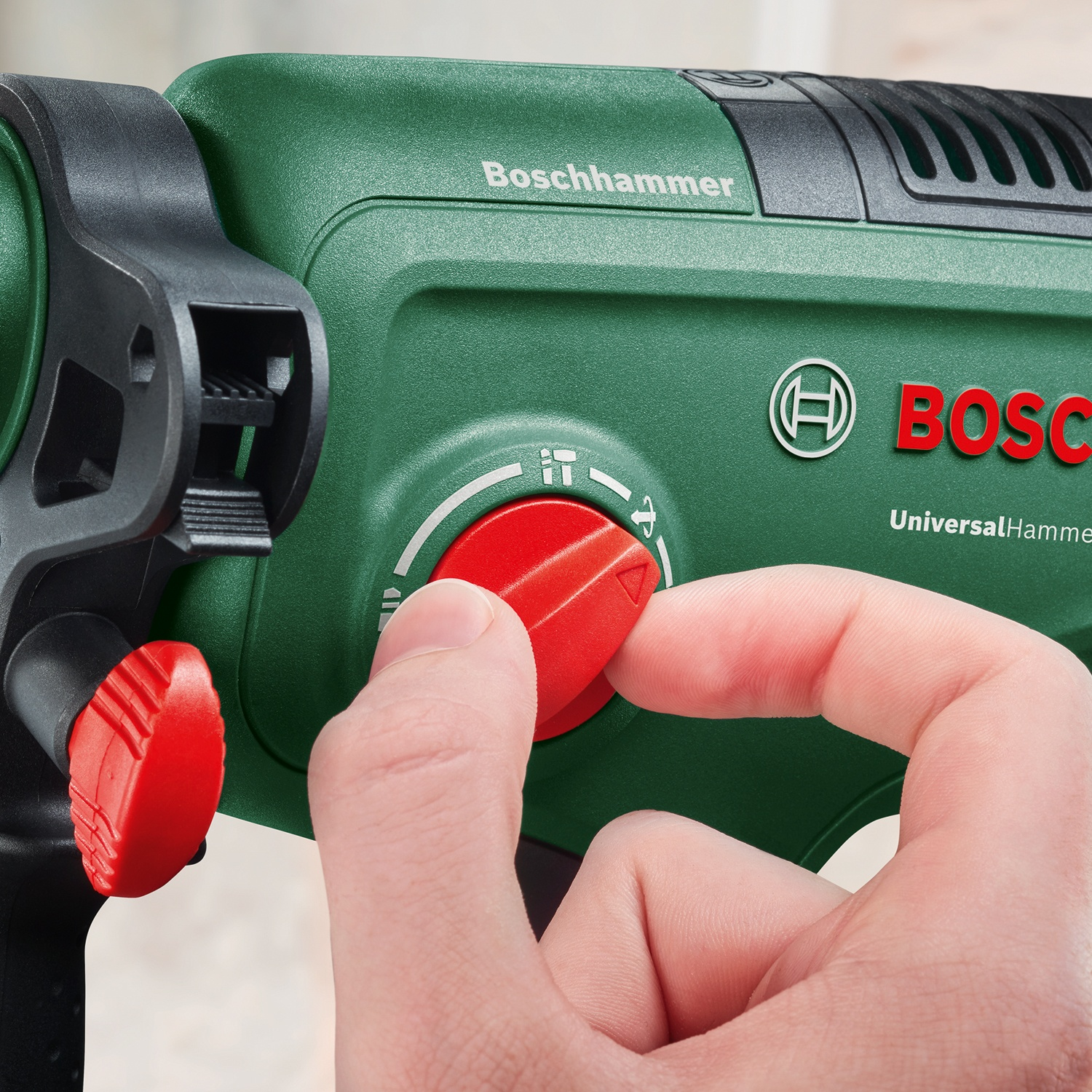 Una mano regola un quadrante rosso su un trapano a martello Bosch verde. Il trapano ha il logo Bosch e 'Boschhammer' stampato sopra.