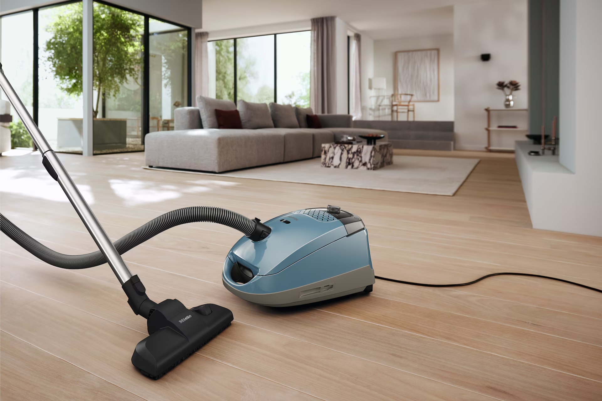 Una aspiradora azul sobre un suelo de madera en una sala de estar moderna. Un sofá es visible en el fondo.