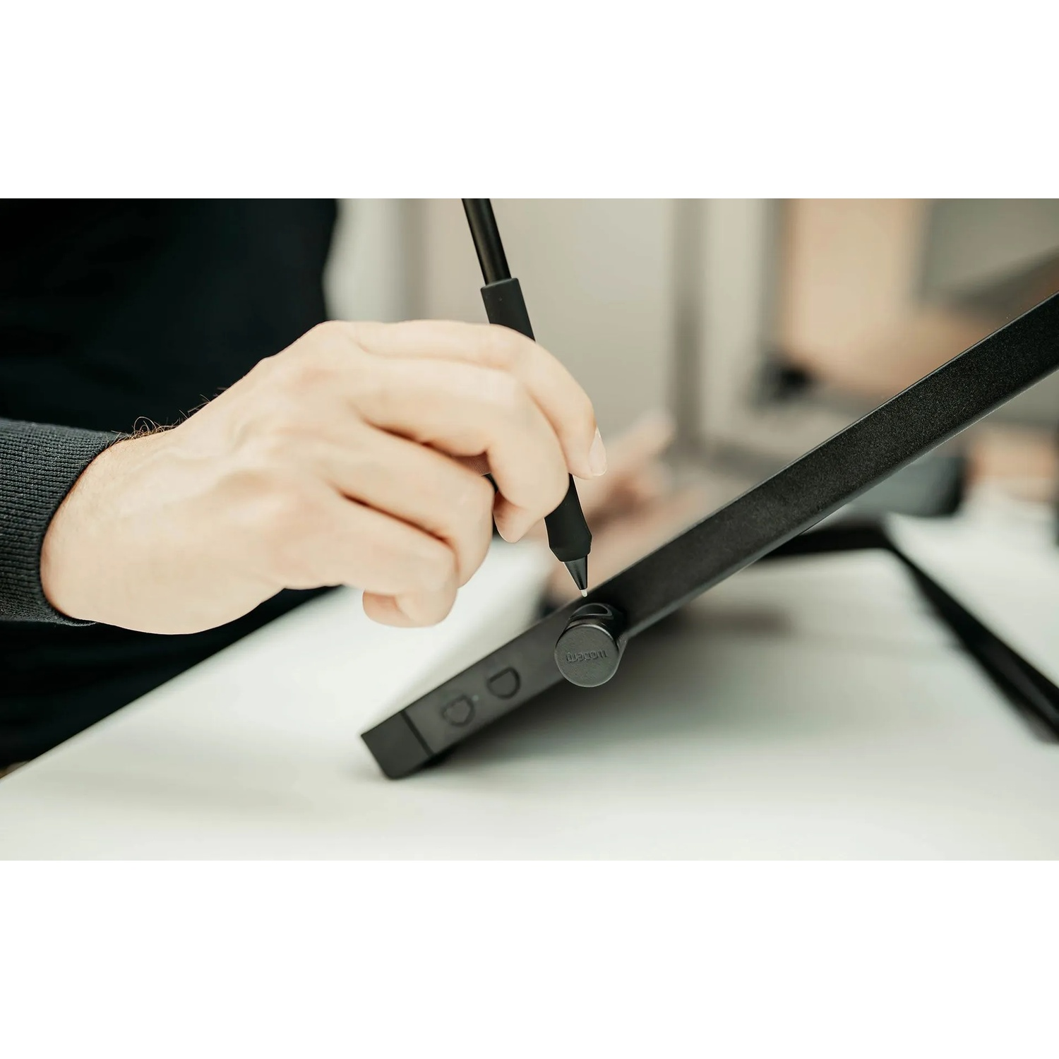 Una mano tiene una penna nera su un tablet nero. Il tablet è su una superficie bianca.