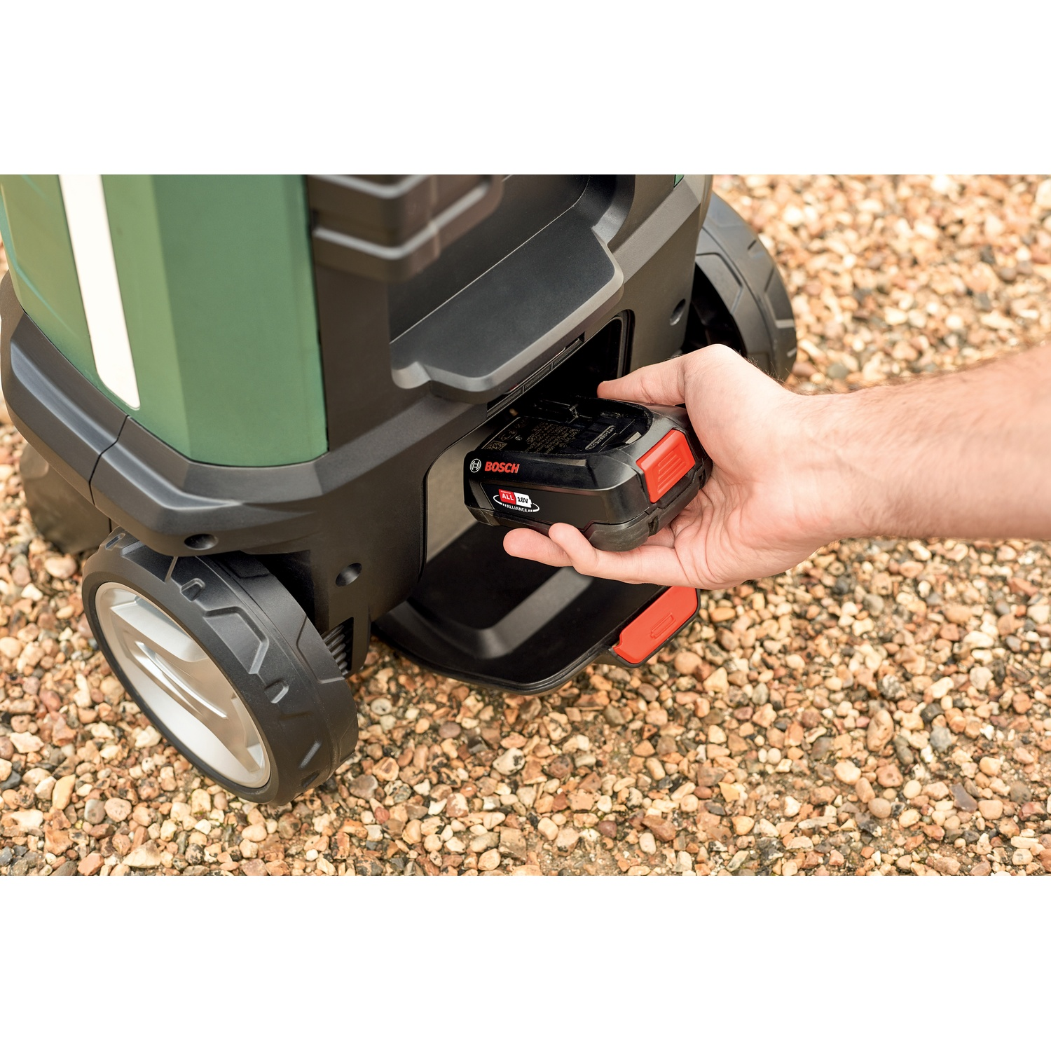 Una persona inserisce una batteria Bosch nera e rossa in una macchina verde e nera su una superficie di ciottoli.