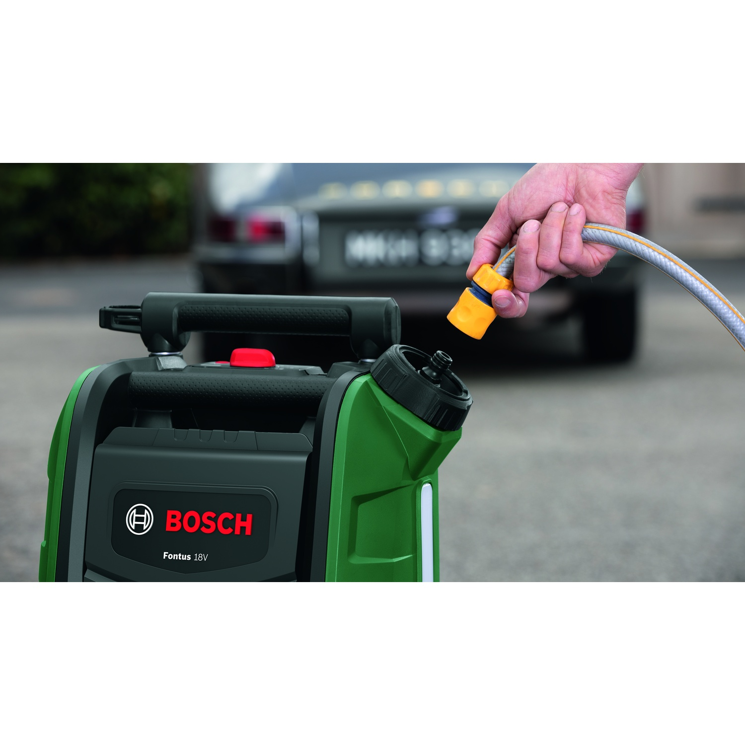 Una pompa dell'acqua Bosch verde e nera con un tubo collegato da una mano. Un'auto è sullo sfondo sfocato.
