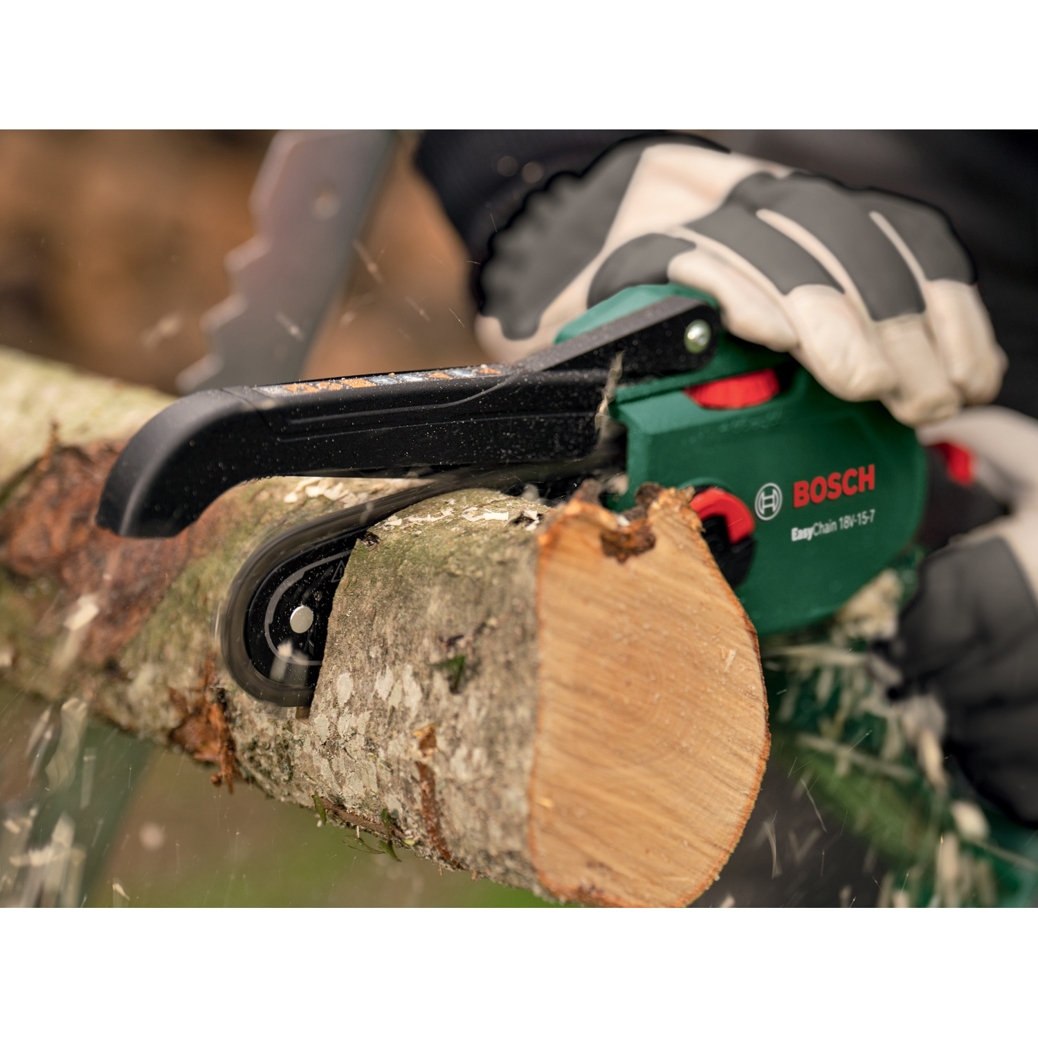 Una persona usa una motosega Bosch verde per tagliare un tronco di legno. Segatura che vola. La persona indossa guanti.