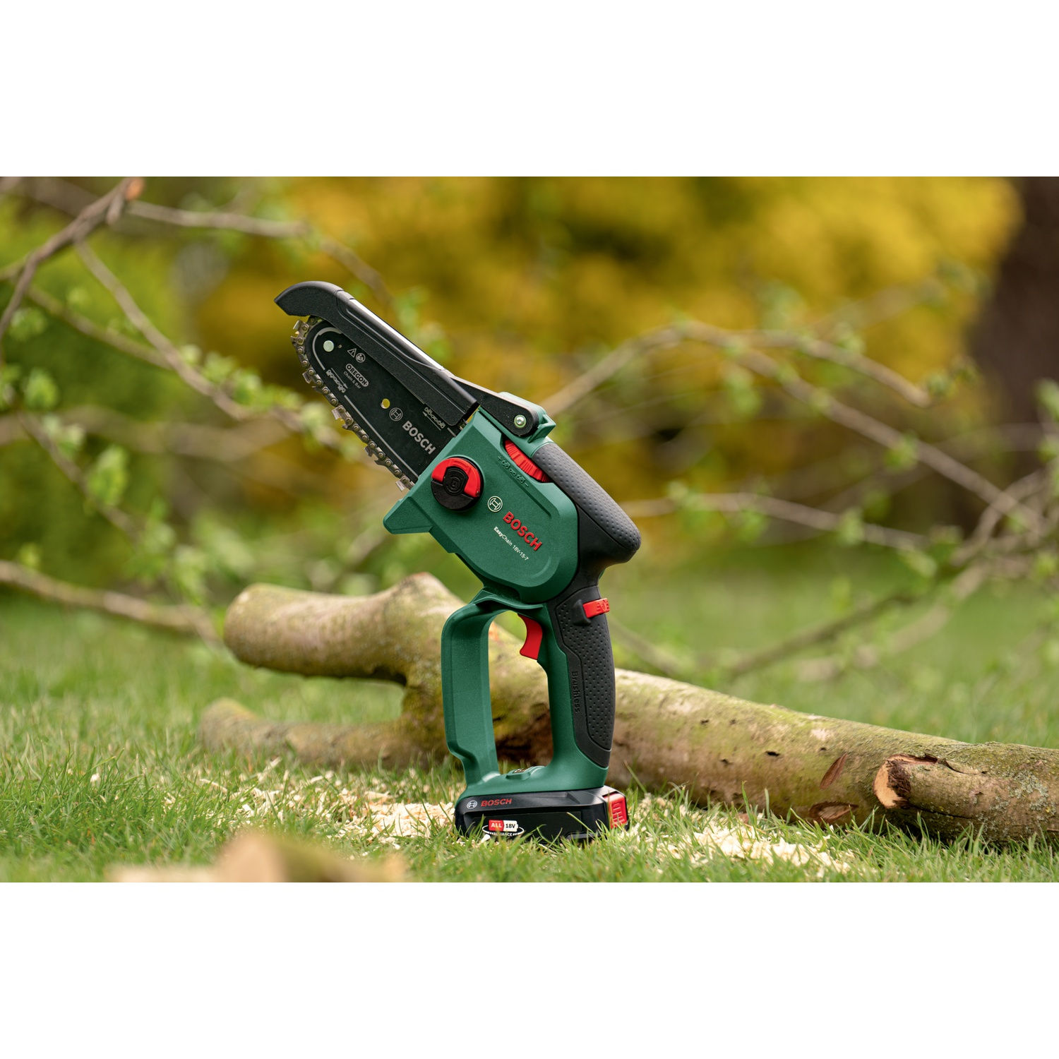 Una motosega Bosch verde e nera è appoggiata sull'erba accanto a un tronco tagliato. Segatura sparsa. Lo sfondo ha un fogliame verde sfocato.