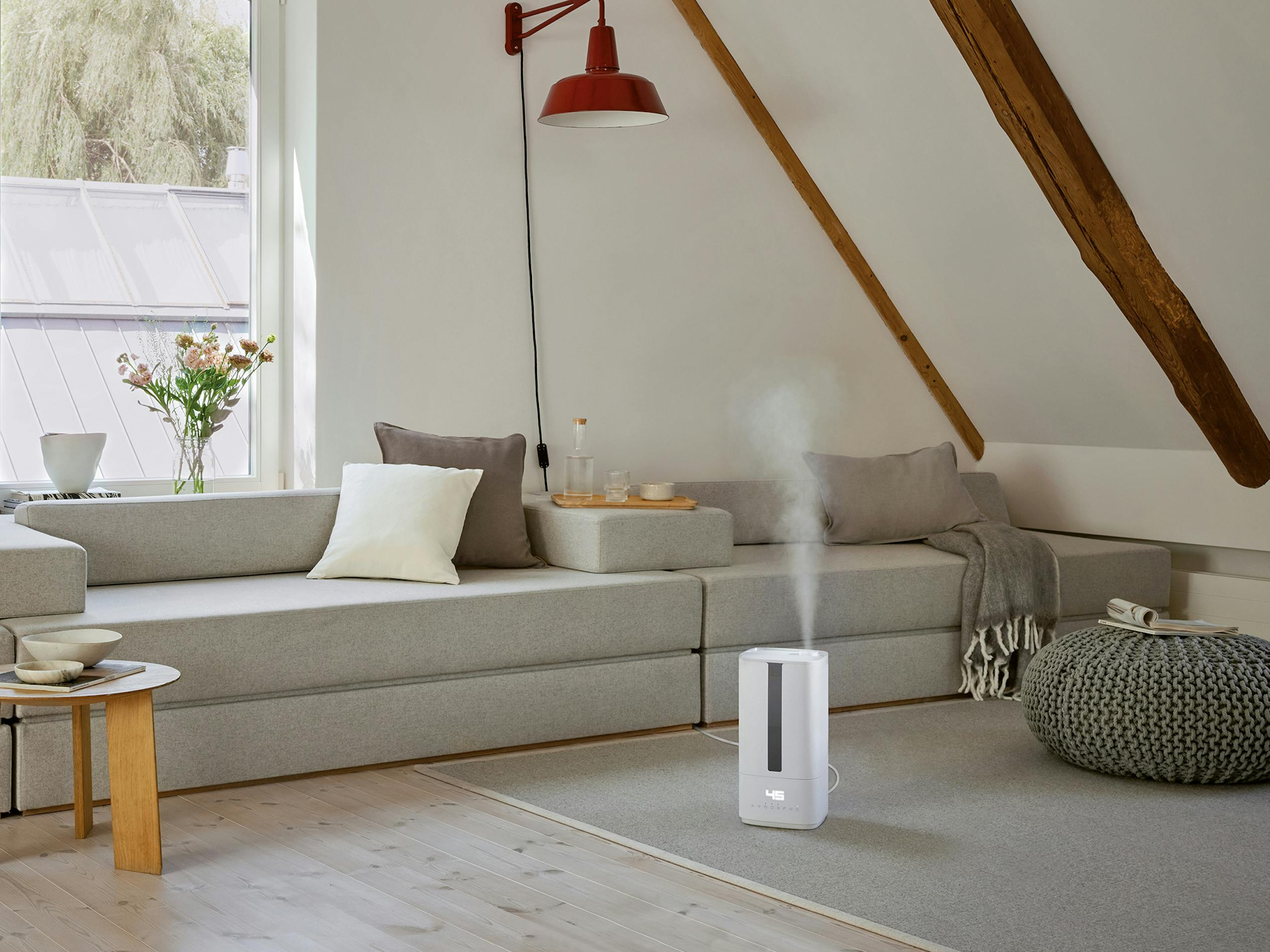 Una stanza moderna con umidificatore, divano, lampada rossa e finestra. Ha travi in legno e tappeto grigio.