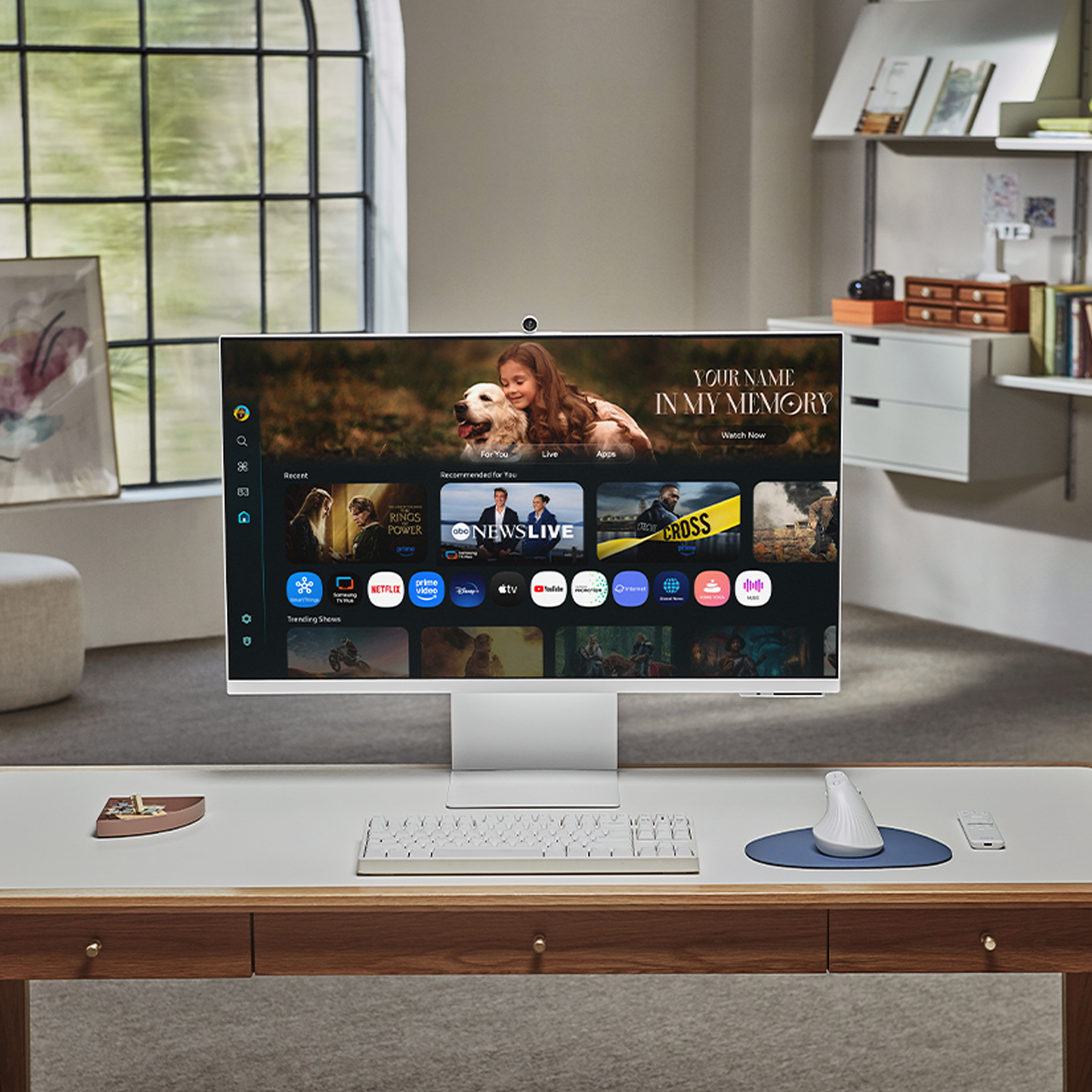 Nowoczesne biurko z dużym monitorem wyświetlającym treści streamingowe. Obecna jest również klawiatura, mysz i pilot.