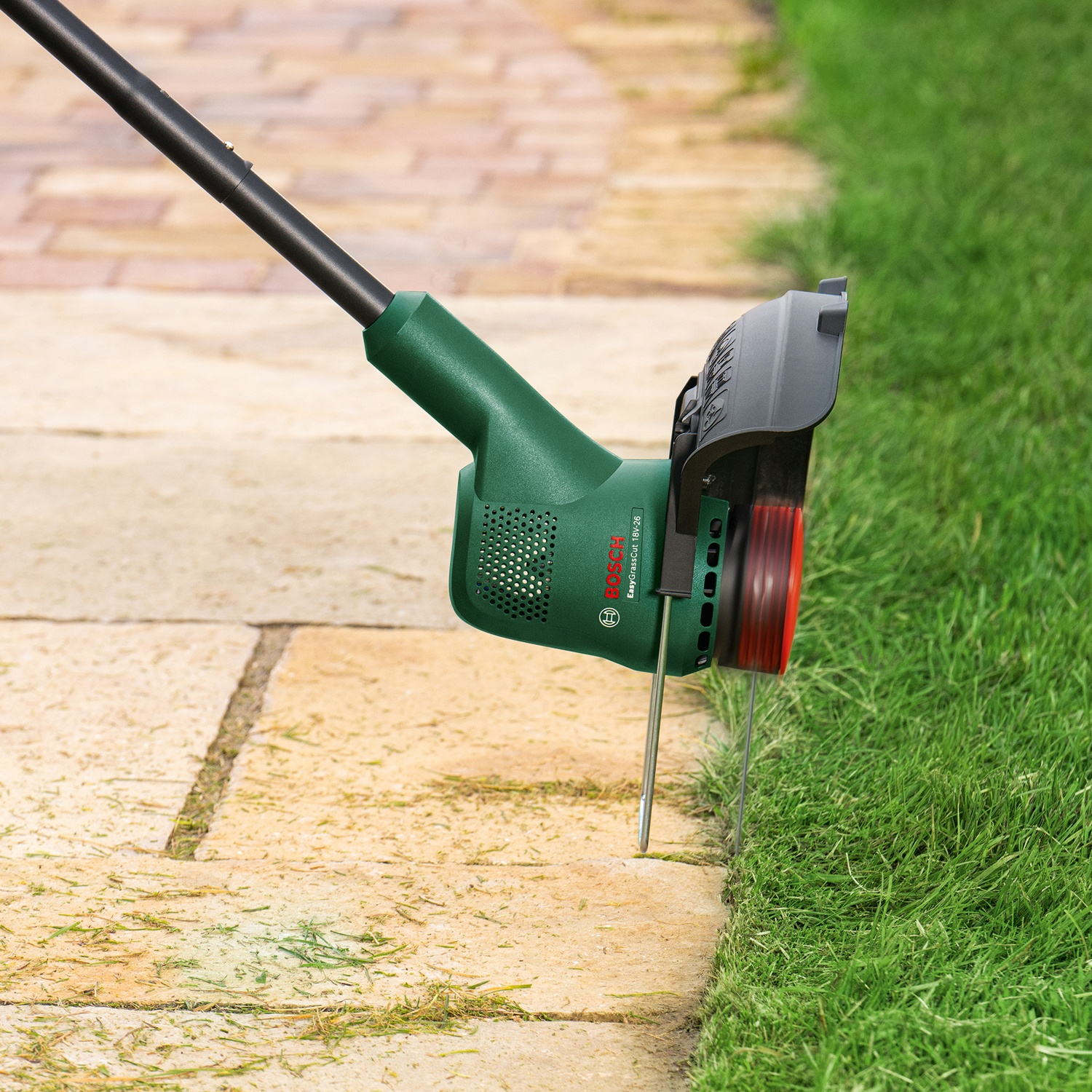 Un tagliaerba Bosch verde e nero sta bordando un prato. Il tagliaerba sta tagliando l'erba lungo il bordo di un vialetto di pietra.