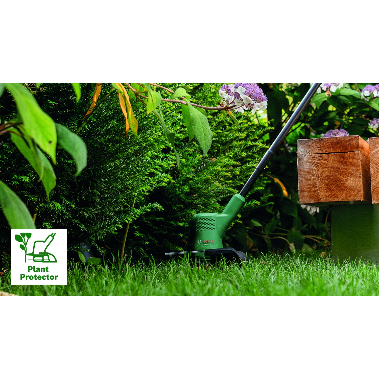 Un tagliaerba verde, un cartello di protezione delle piante e una panchina di legno sono a fuoco. Lo sfondo ha cespugli e un fiore.