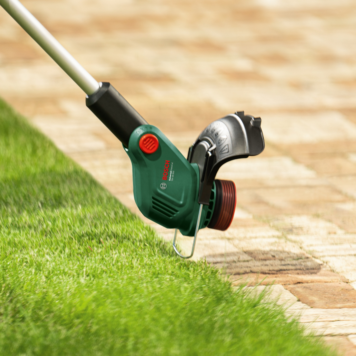 Un tagliaerba verde e nero taglia l'erba. Sentiero di mattoni sullo sfondo. Il tagliaerba è di marca Bosch.