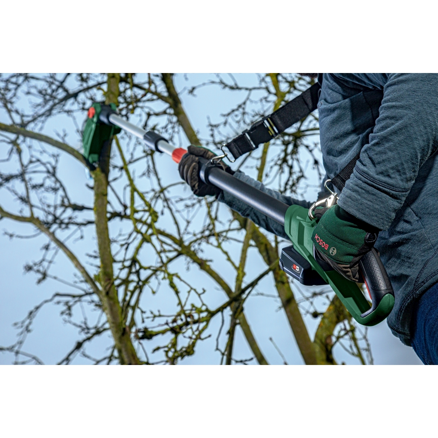 Una persona usa una sega a palo verde e nera per potare un albero. La sega ha una punta rossa e viene tenuta con mani guantate.