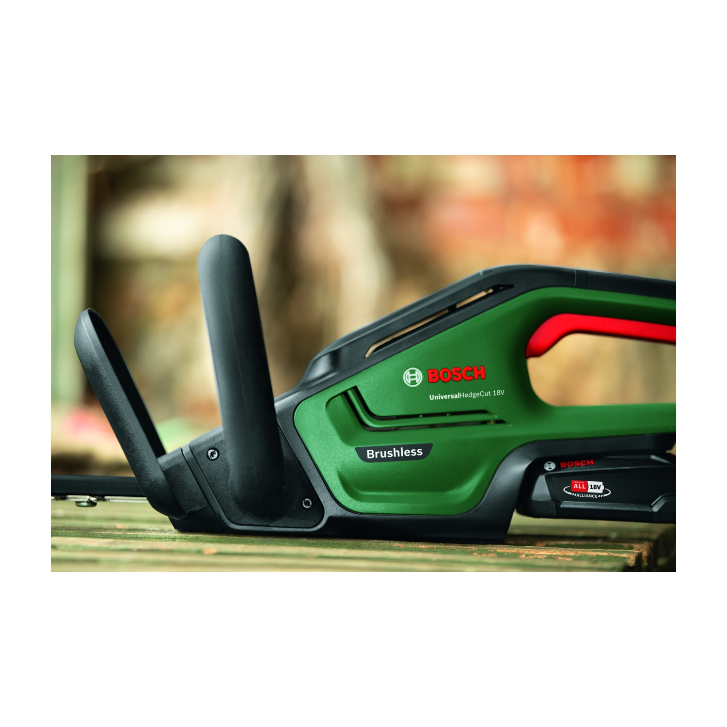 Un tagliasiepi Bosch verde su una superficie di legno. Manici neri, dettagli rossi. Lo sfondo è sfocato, con foglie e legno.