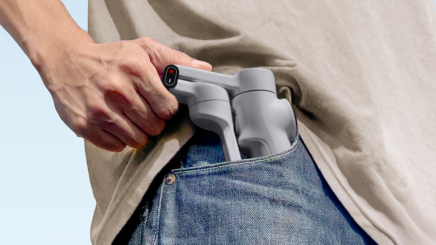 Una mano coloca un estabilizador gris en un bolsillo de mezclilla azul. La persona lleva una camisa beige.